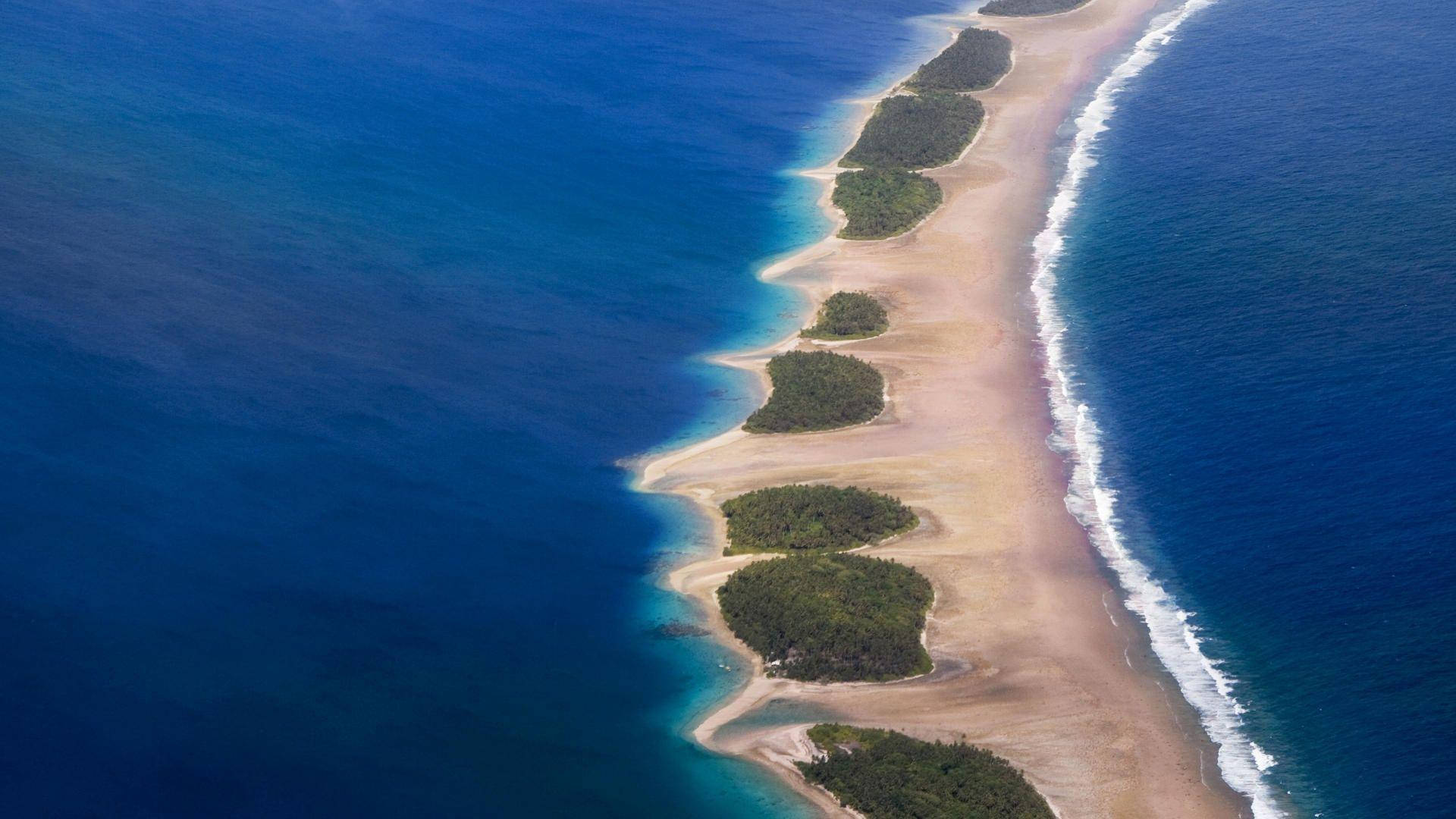 馬紹爾群島沙洲 壁紙 — 從高空俯瞰一條長長的沙質屏障島，島上有茂密的綠色斑塊，分隔著深藍色的海洋水域。