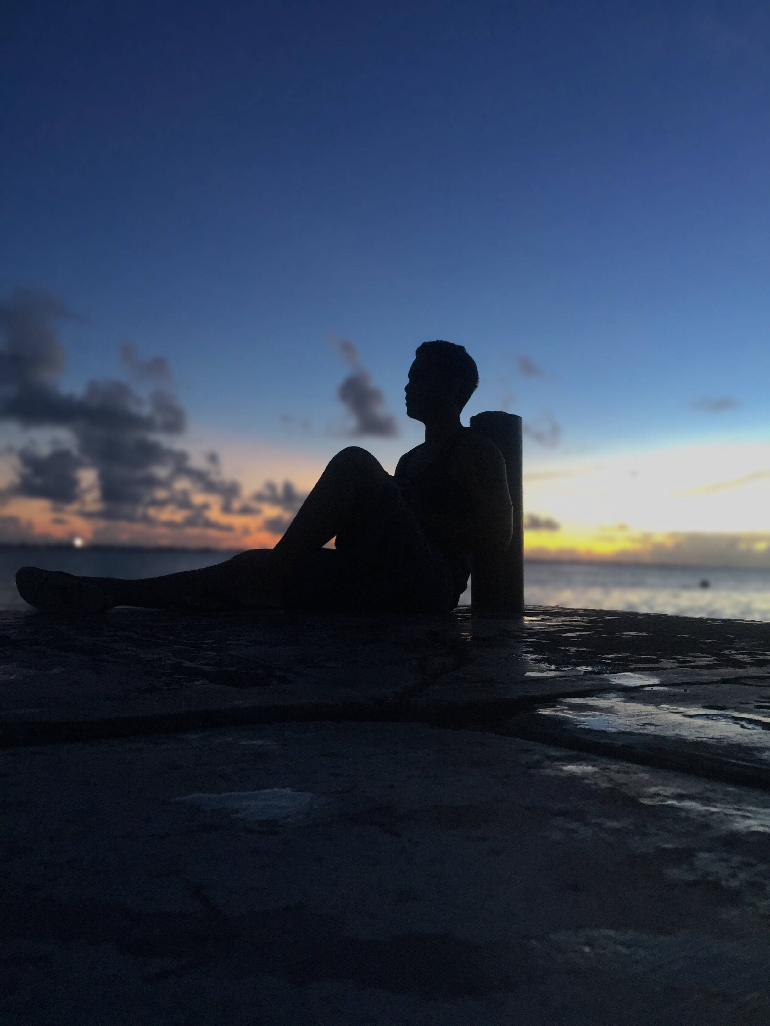 馬紹爾群島海灘夜間人影 壁紙 — 一個人的剪影，在黃昏時獨自坐在碼頭上，背後是充滿活力的橙色和藍色天空。