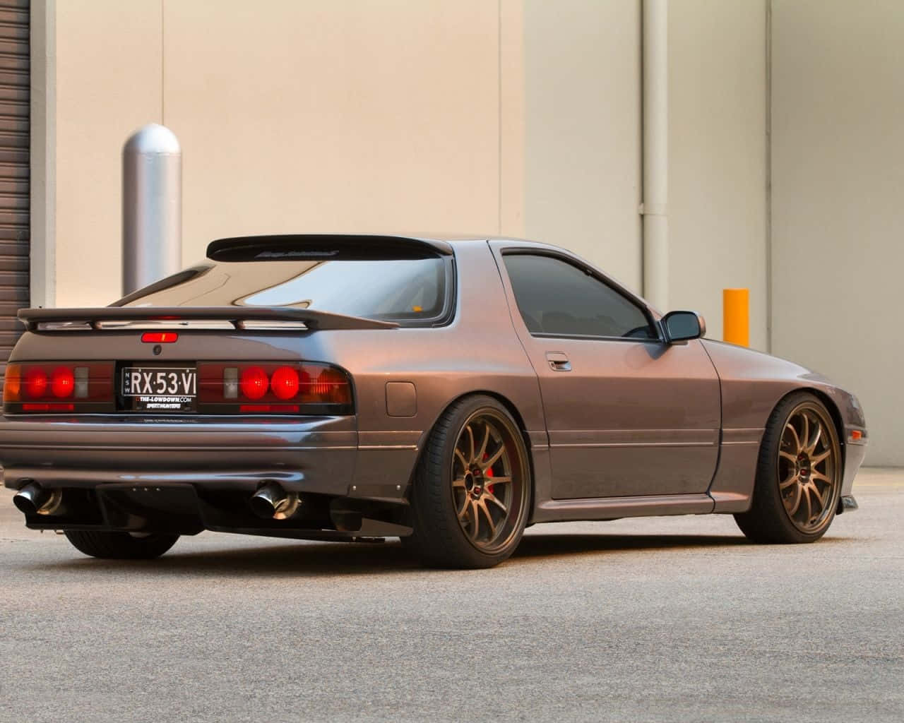 青銅色日產240SX跑車，紅色尾燈，停在米色建築附近。