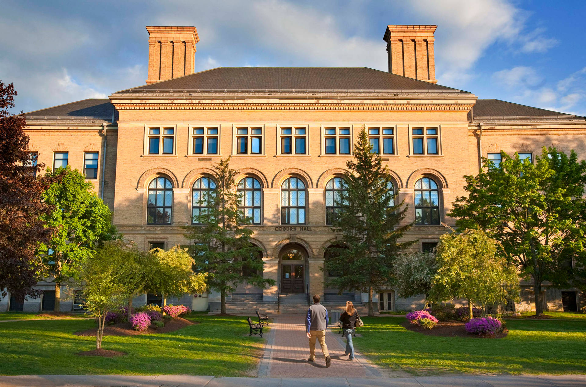 兩個學生在陽光明媚的校園日走向一座歷史悠久的大學建築。