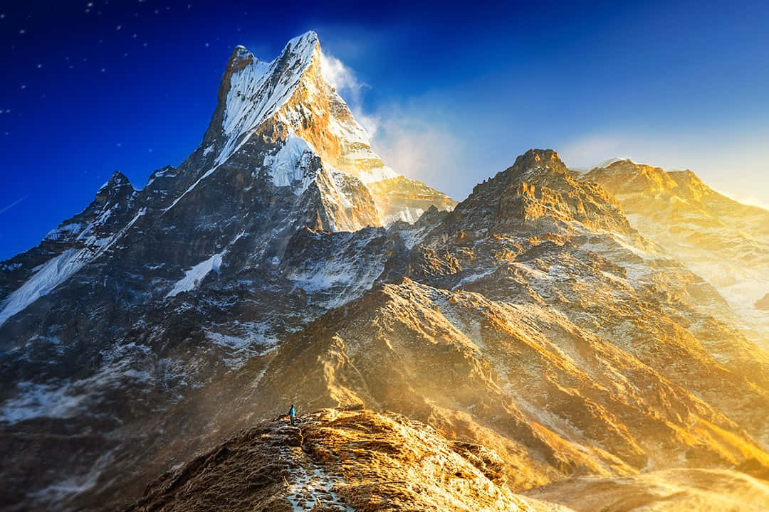 日出時山脊上的一個小小登山者，有積雪的山峰和星空。