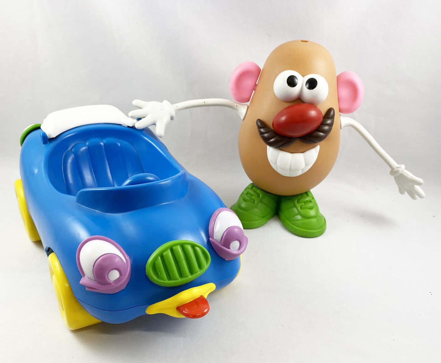 Mr. Potato Head 玩具旁邊有一輛色彩繽紛的塑膠車。