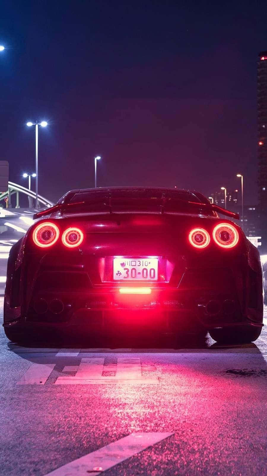 夜間潮濕城市街道上帶有紅色尾燈的黑色跑車。