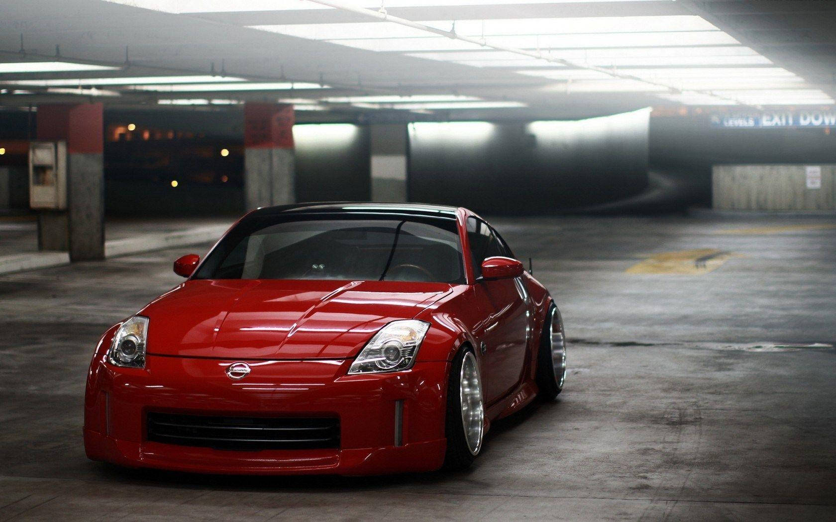 駕馭 Nissan 350Z — 生活的極速 壁紙 — 一架亮麗紅色日產350Z跑車，降低懸掛，戲劇性地停泊在燈光昏暗的地下停車場。