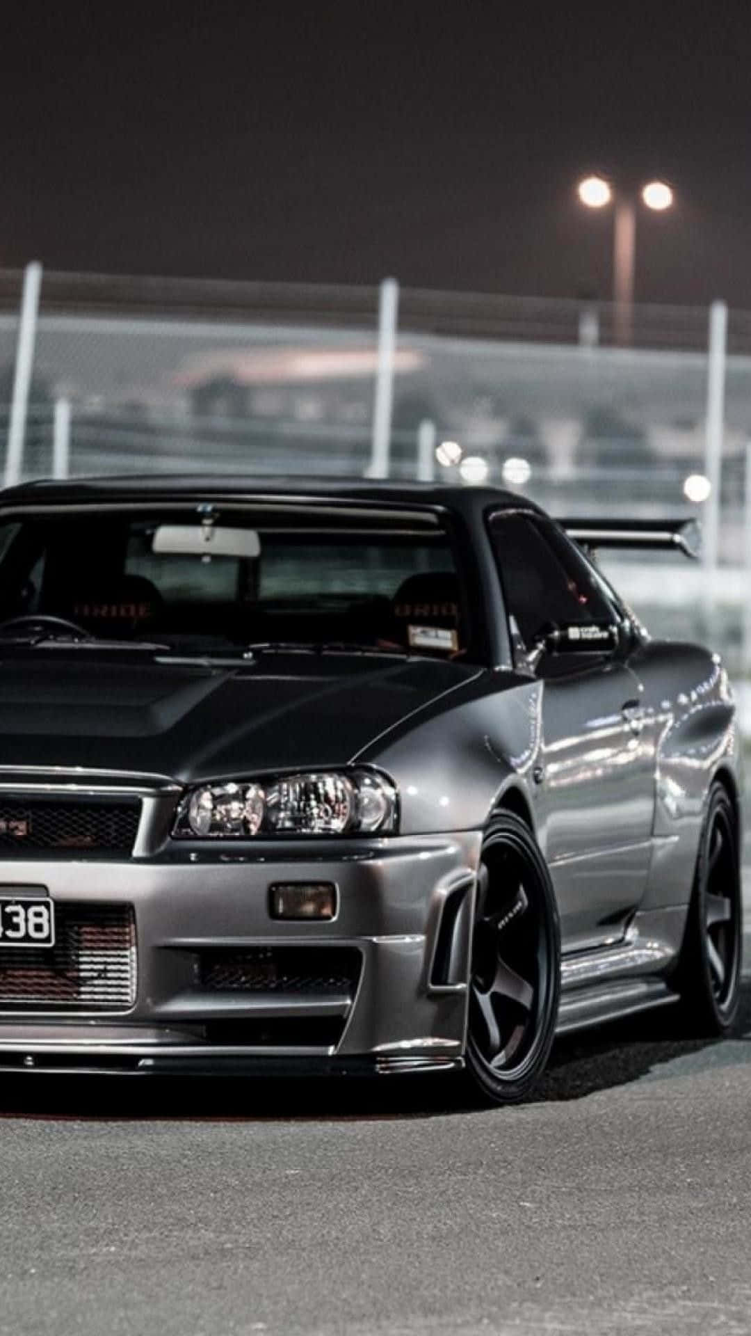 銀色日產Skyline R34在夜間賽道上，在明亮燈光下。