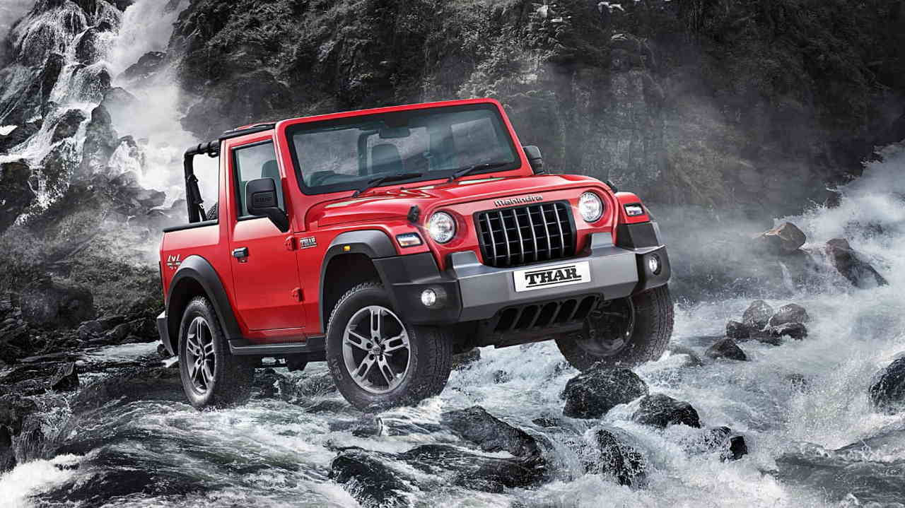 紅色 Mahindra Thar SUV 在岩石上奔騰的河水中行駛。