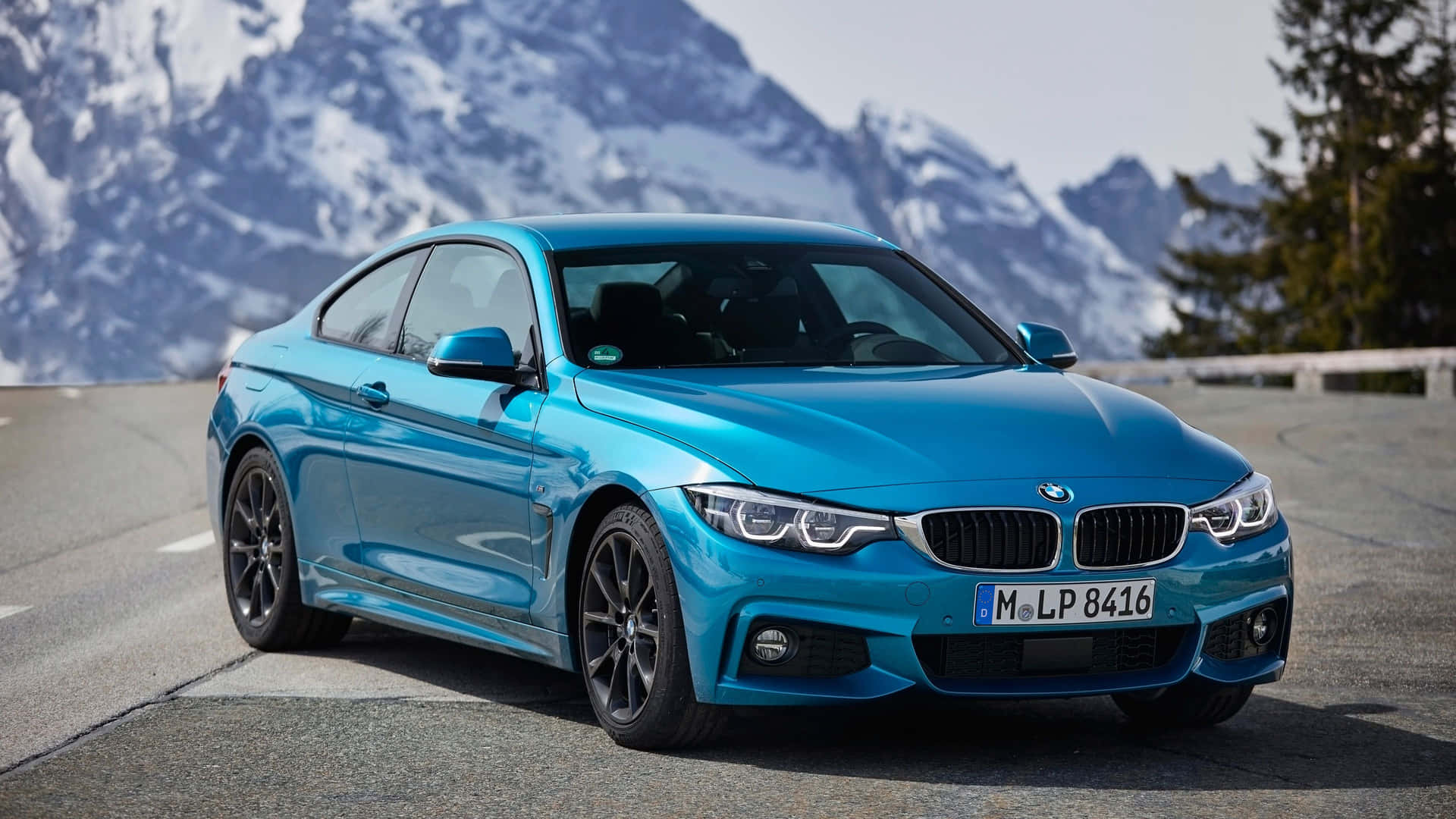藍色BMW雙門跑車停在山路上，後面有雪峰。