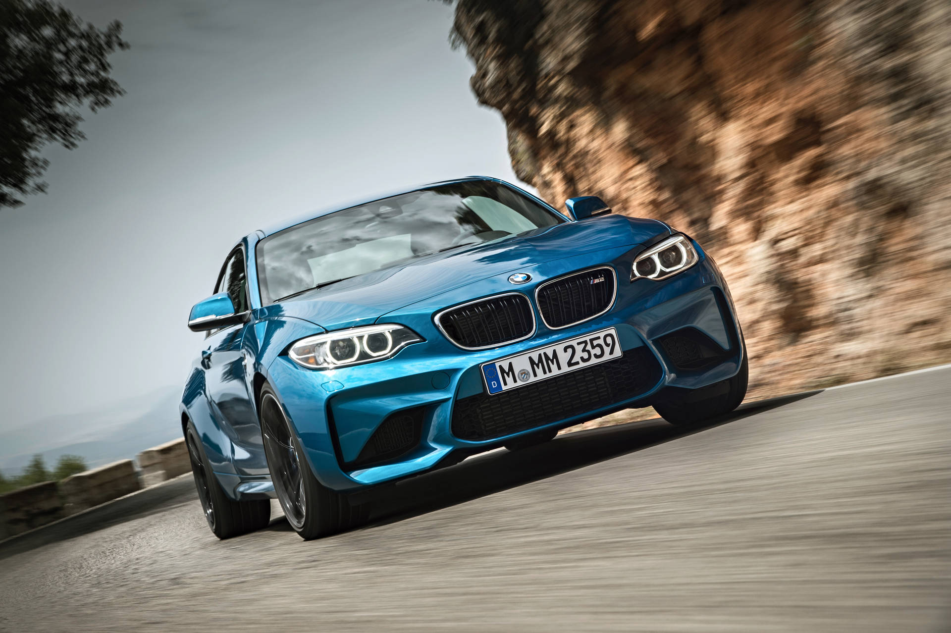 藍色BMW M2 Coupe在山路上疾馳，帶有模糊動態效果。