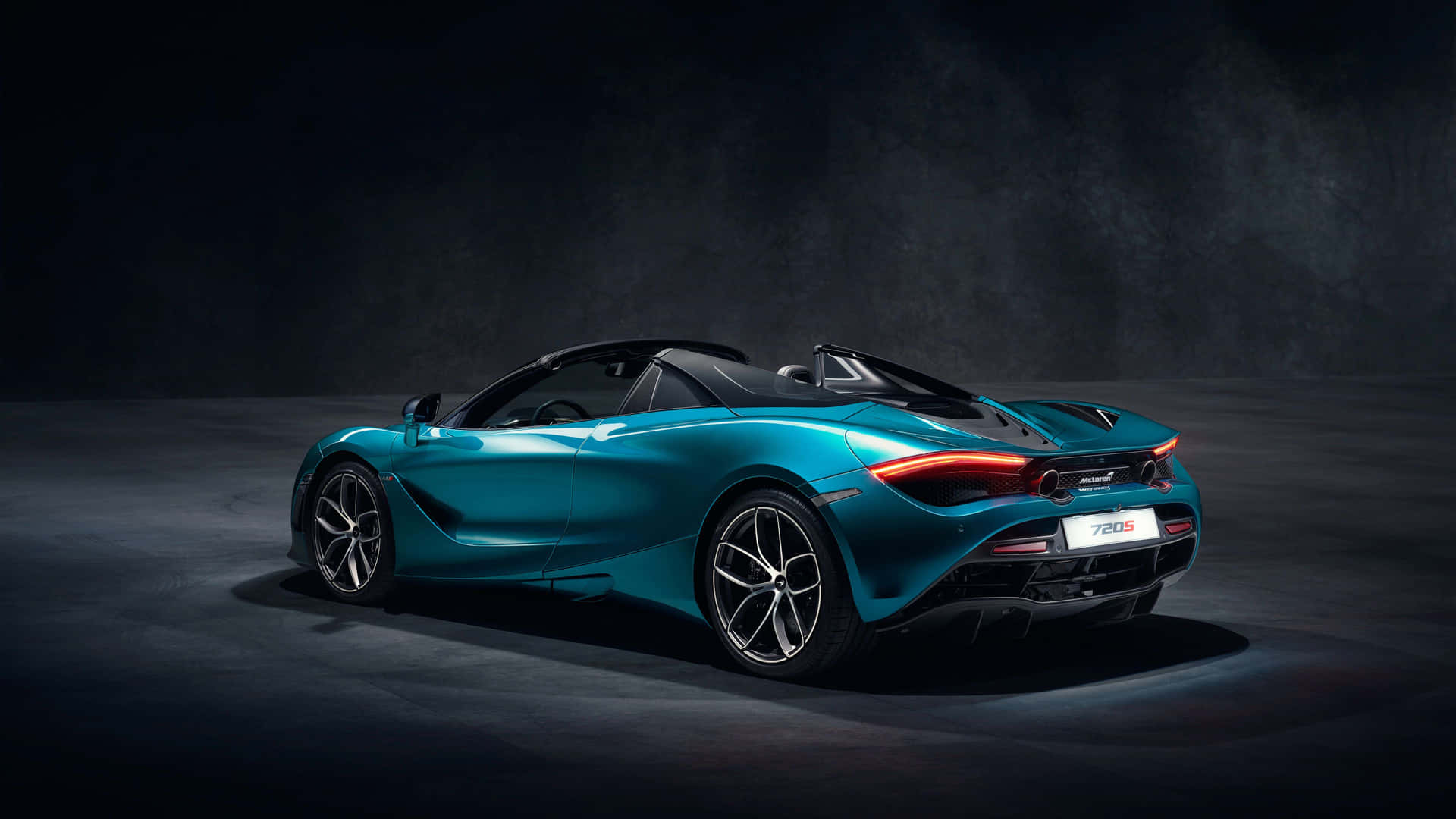 在攝影棚中，戲劇性燈光下的藍綠色McLaren 720S Spider開篷跑車。