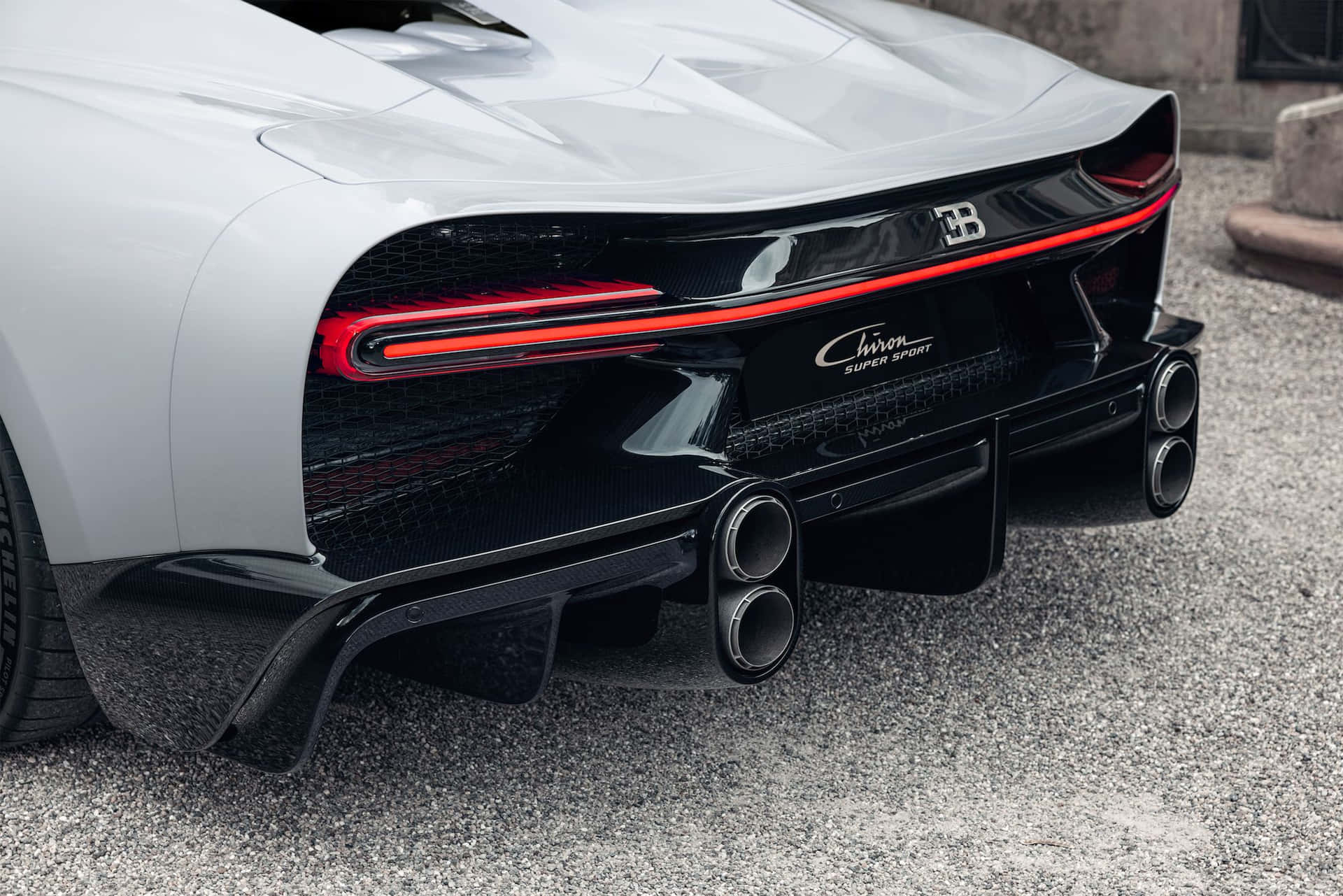 白色布加迪Chiron Super Sport尾部，帶紅色尾燈和四出排氣管，在礫石上。