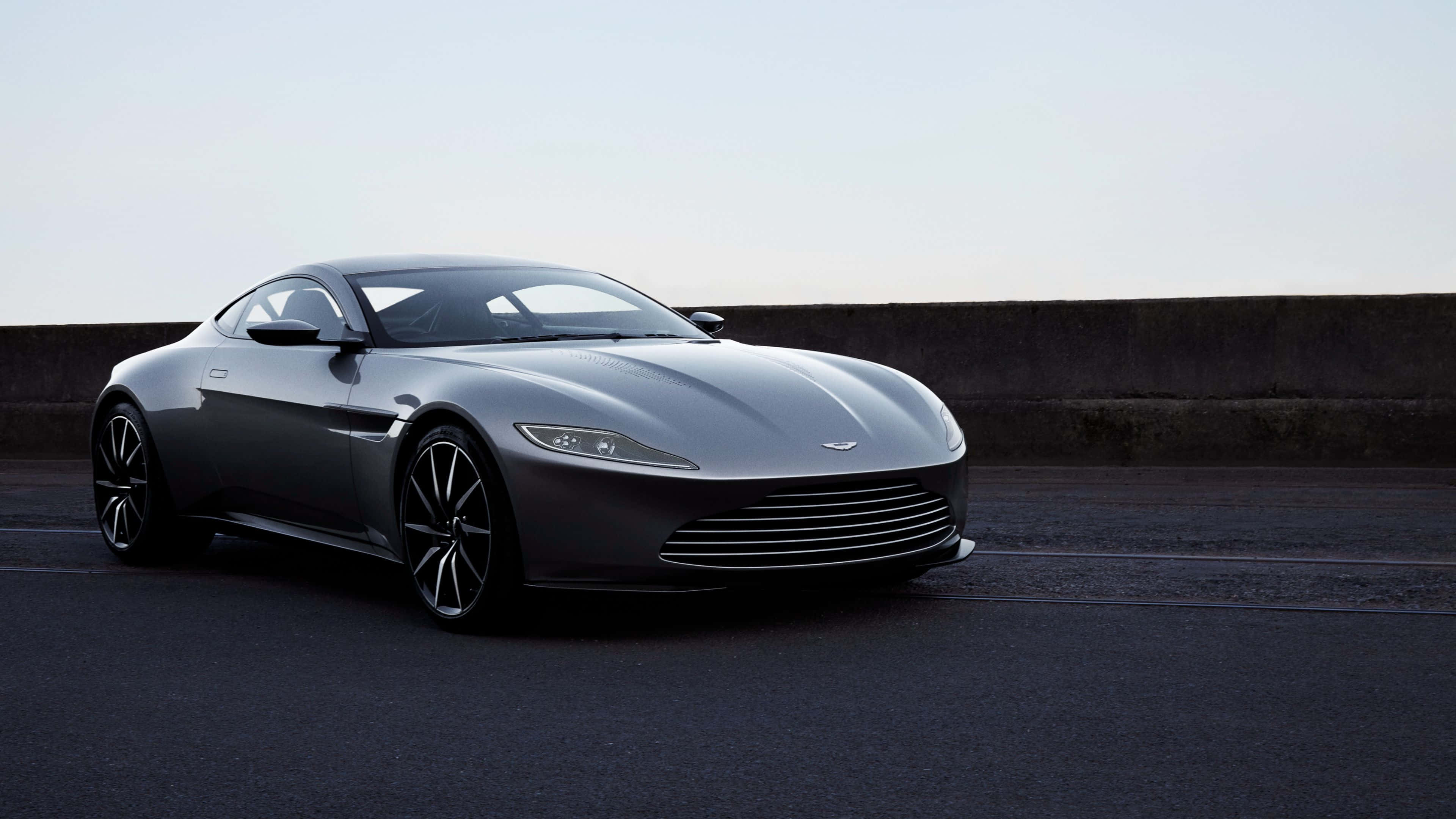 駕馭奢華與時尚 壁紙 — 一架時尚的銀色Aston Martin跑車停泊在昏暗瀝青路上，旁邊是混凝土護欄，天空蒼白。