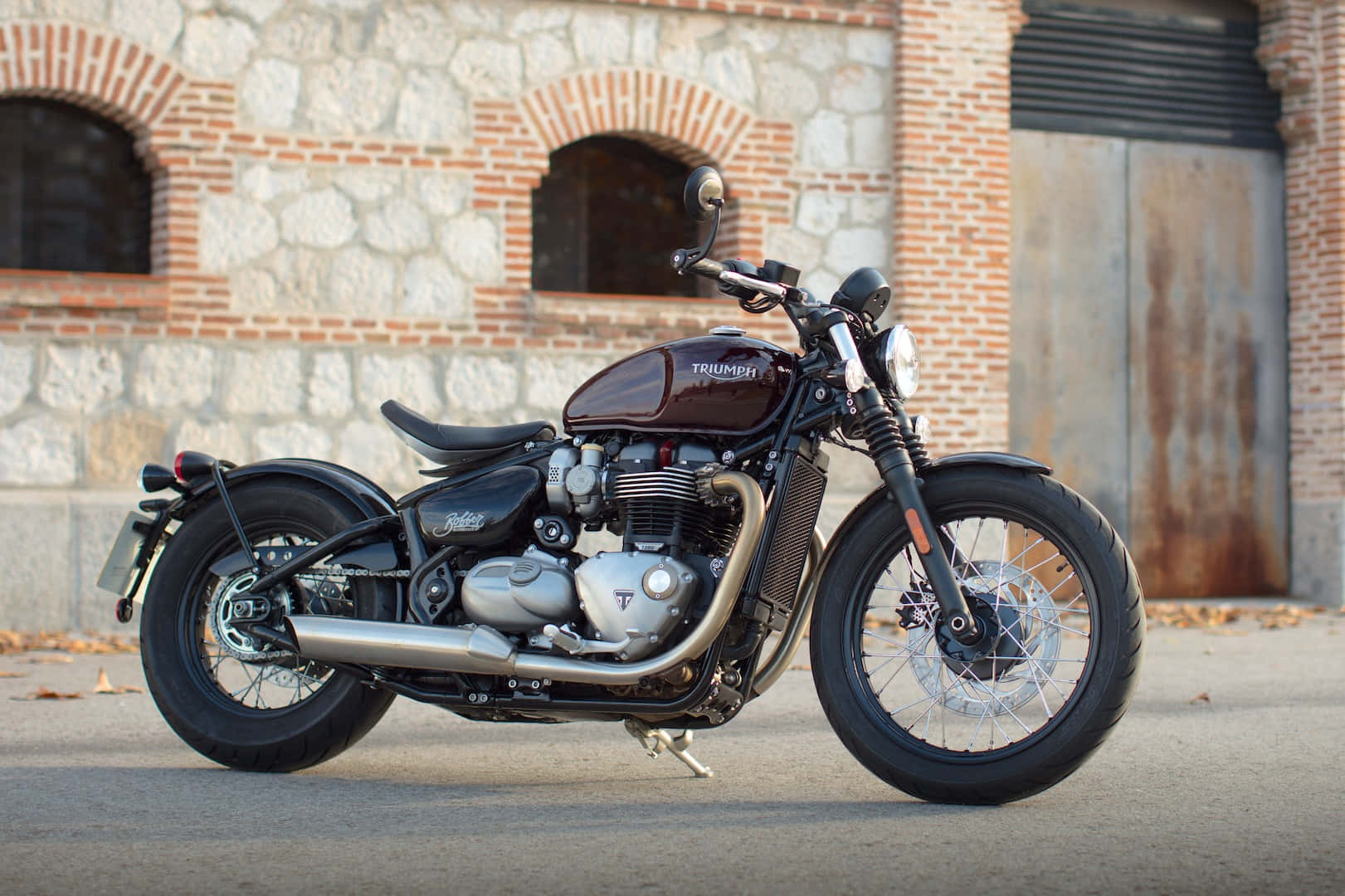 經典栗色 Triumph 電單車停泊在磚石建築前。