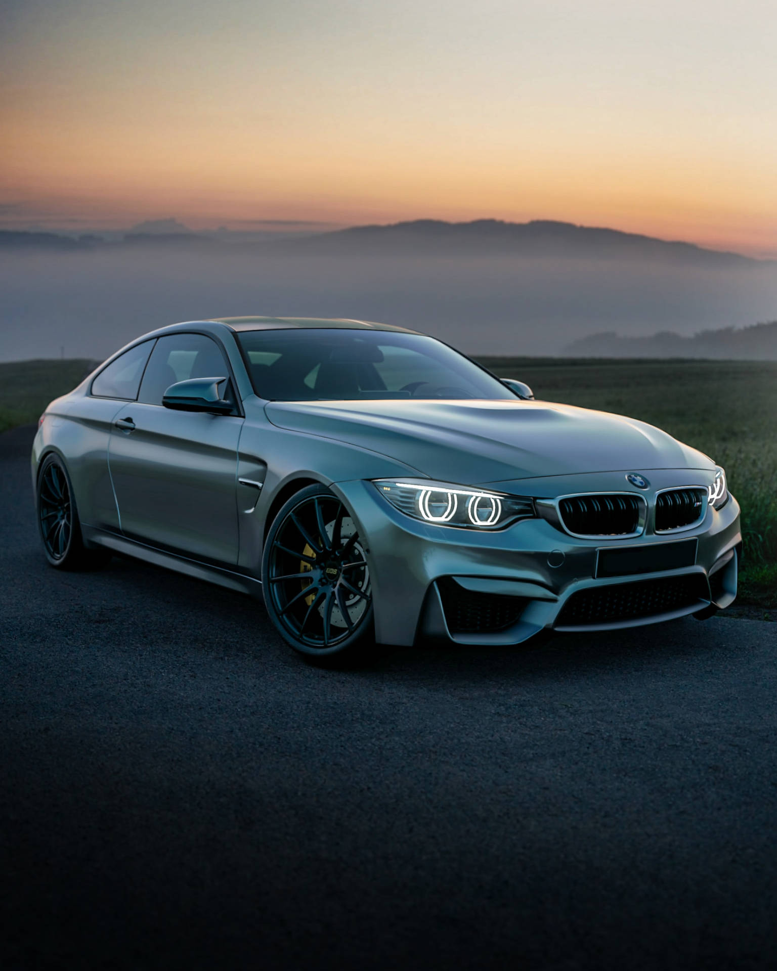 銀色BMW M4跑車在黎明時停泊在霧氣瀰漫的山路上。