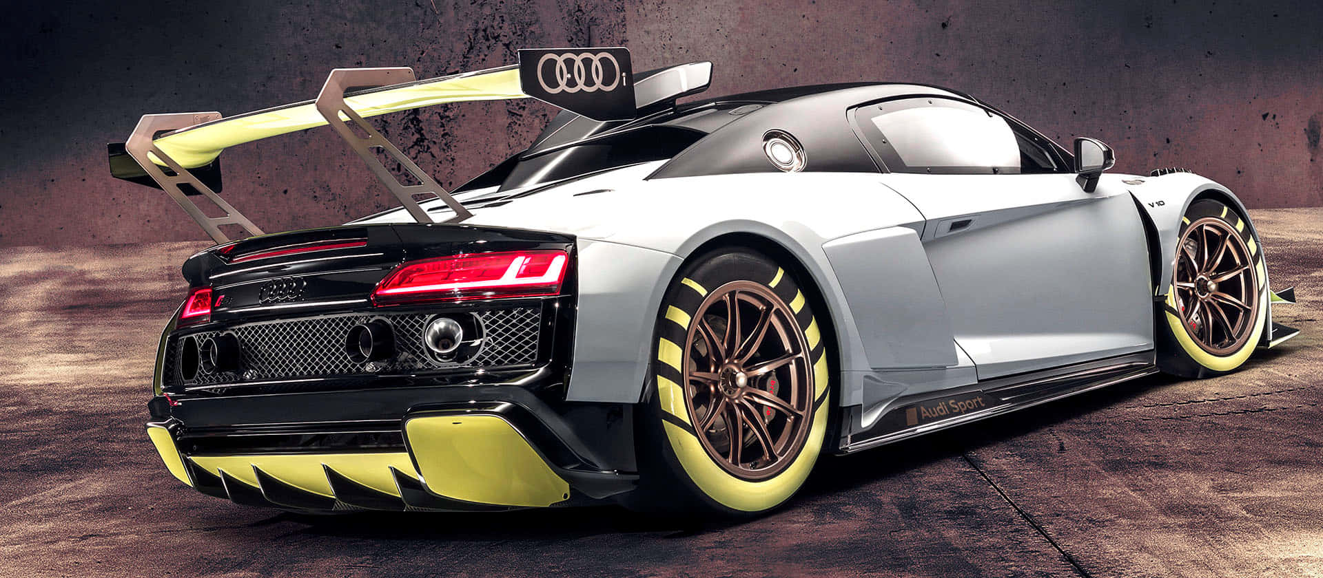 駕馭時尚 壁紙 — 一輛銀色奧迪R8 LMS GT3賽車，帶有黃色點綴和大型尾翼，停在混凝土表面上。