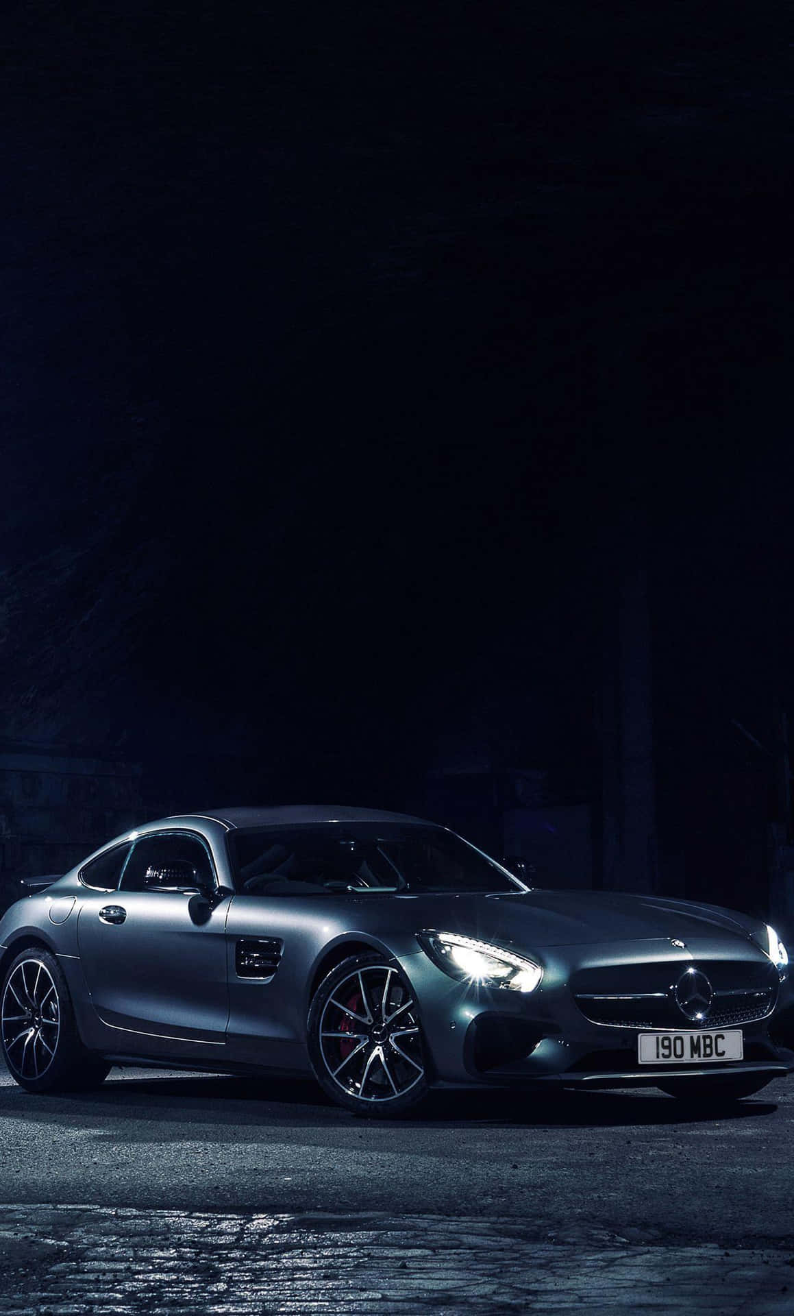 銀色 Mercedes-AMG GT 跑車在黑暗的鵝卵石街道上被車頭燈照亮。