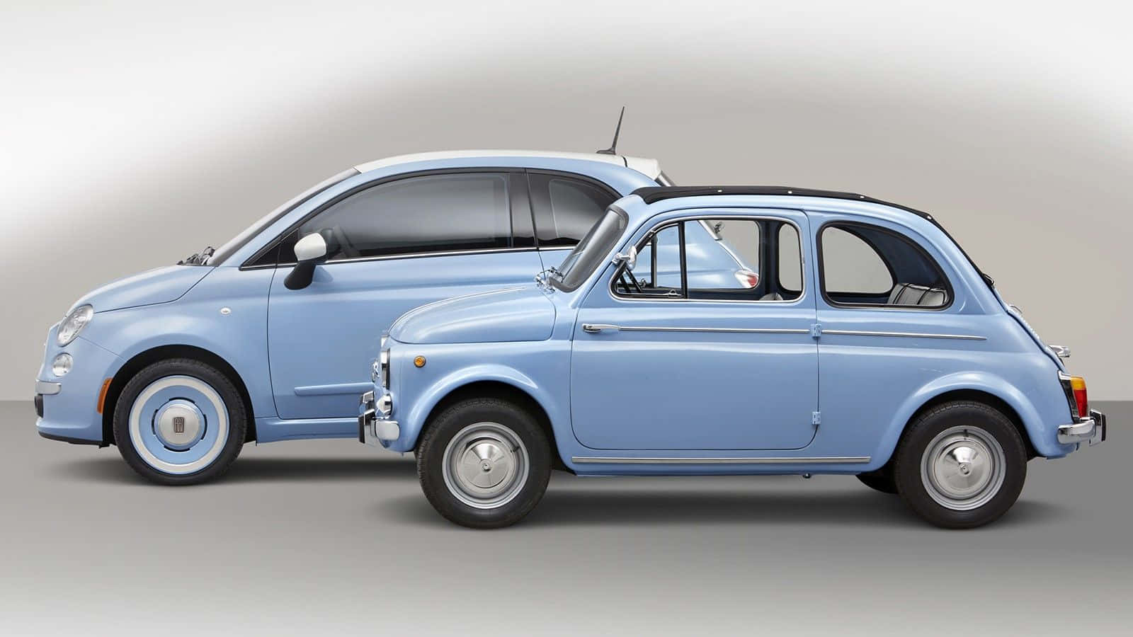 駕馭時尚酷車 壁紙 — 兩輛淺藍色嘅Fiat 500車，一架現代一架經典，並排喺中性嘅工作室背景上。