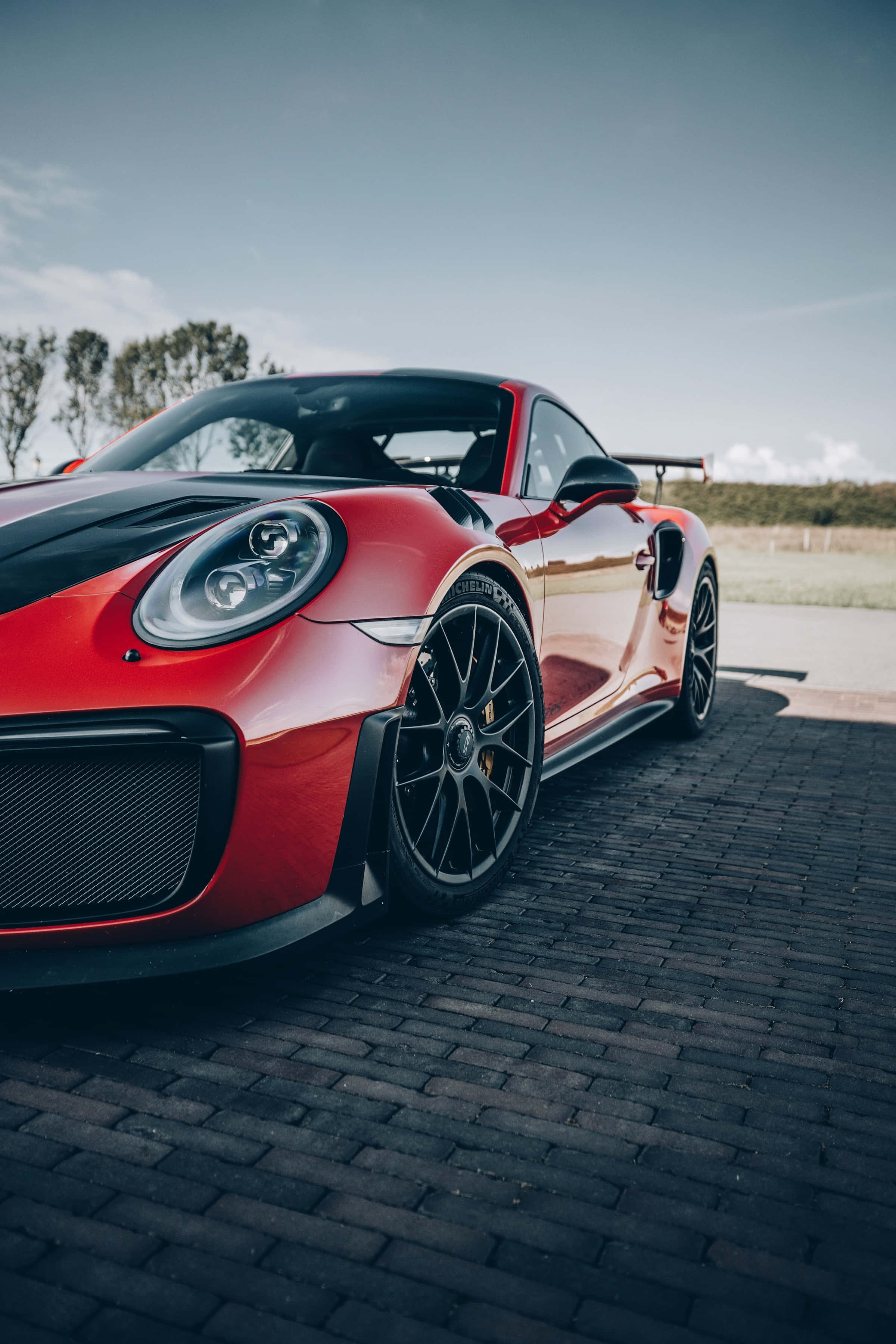 駕馭時尚風采 壁紙 — 一輛充滿活力的紅色保時捷911 GT2 RS，帶有黑色點綴，停泊在晴朗天空下的鵝卵石路面上。