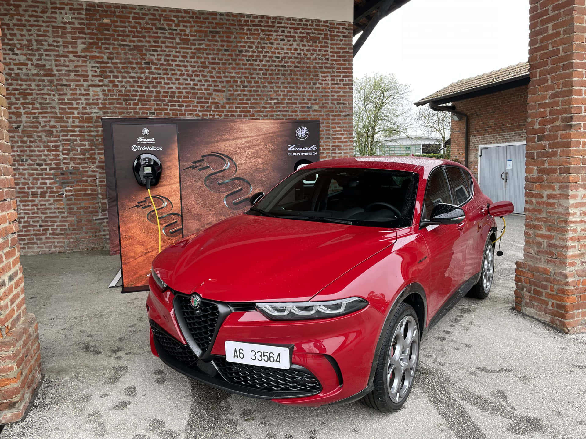 紅色 Alfa Romeo Tonale 電動 SUV 插入磚砌建築附近的充電站。