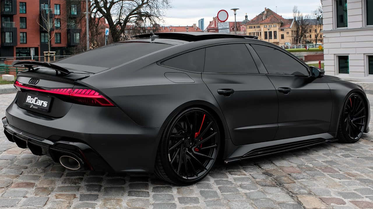啞光黑色奧迪RS7 Sportback，帶紅色點綴，停在鵝卵石街道上。 — 奧迪 GIF 壁紙