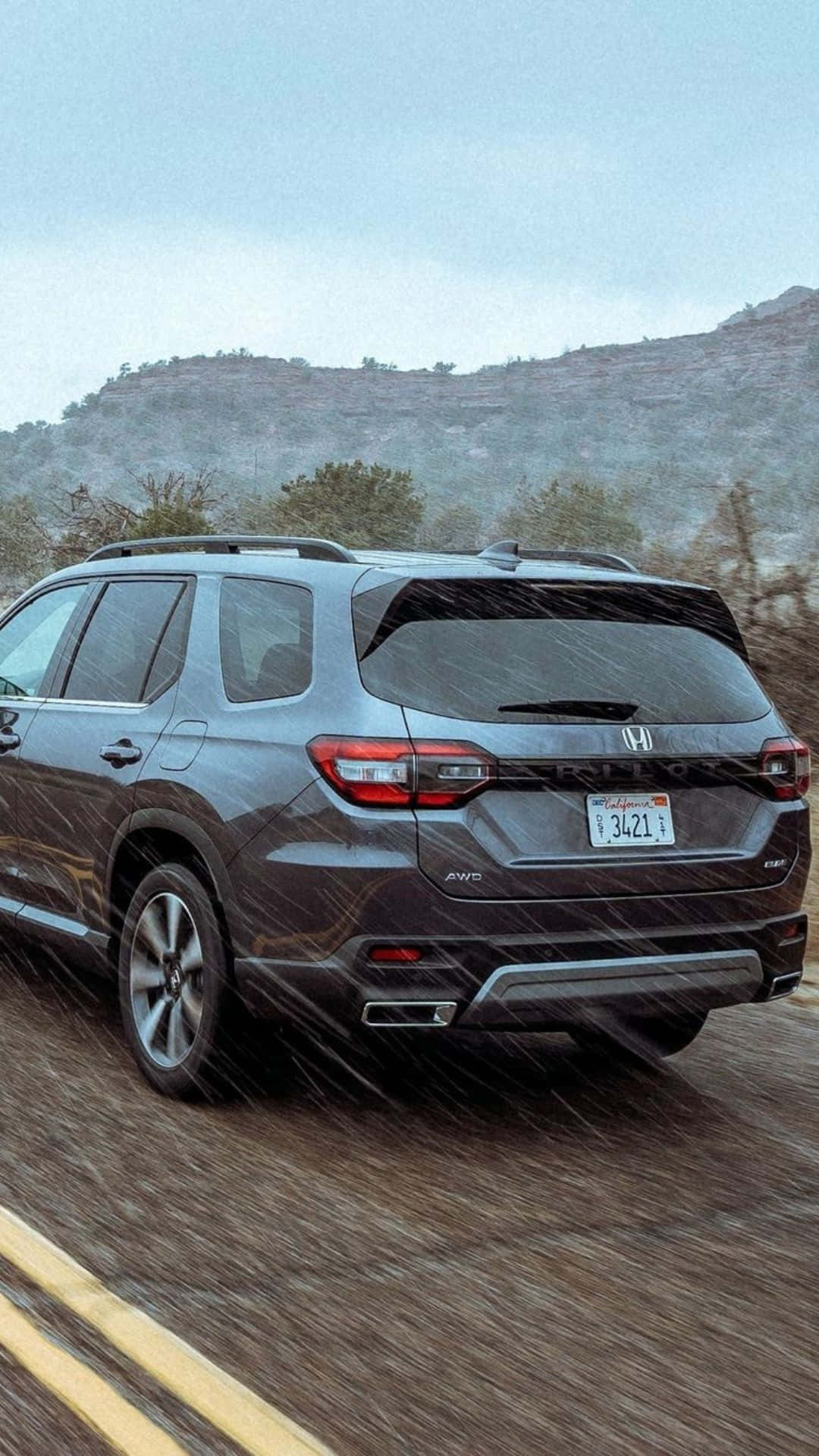 駕馭風采：2023 Honda Pilot 與您探索旅途 壁紙 — 一架灰色本田Pilot SUV在暴雨中行駛於山路，背景有模糊的動態和霧氣籠罩的山丘。