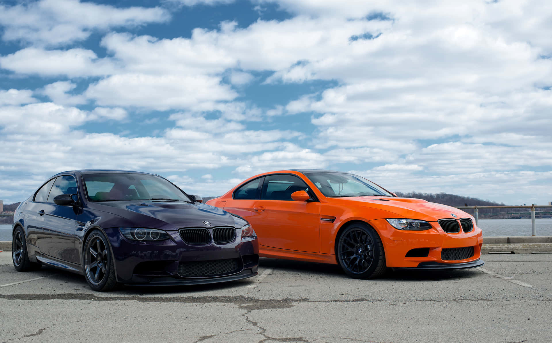 兩輛高性能BMW M3汽車並排停放在瀝青停車場上，天空多雲。