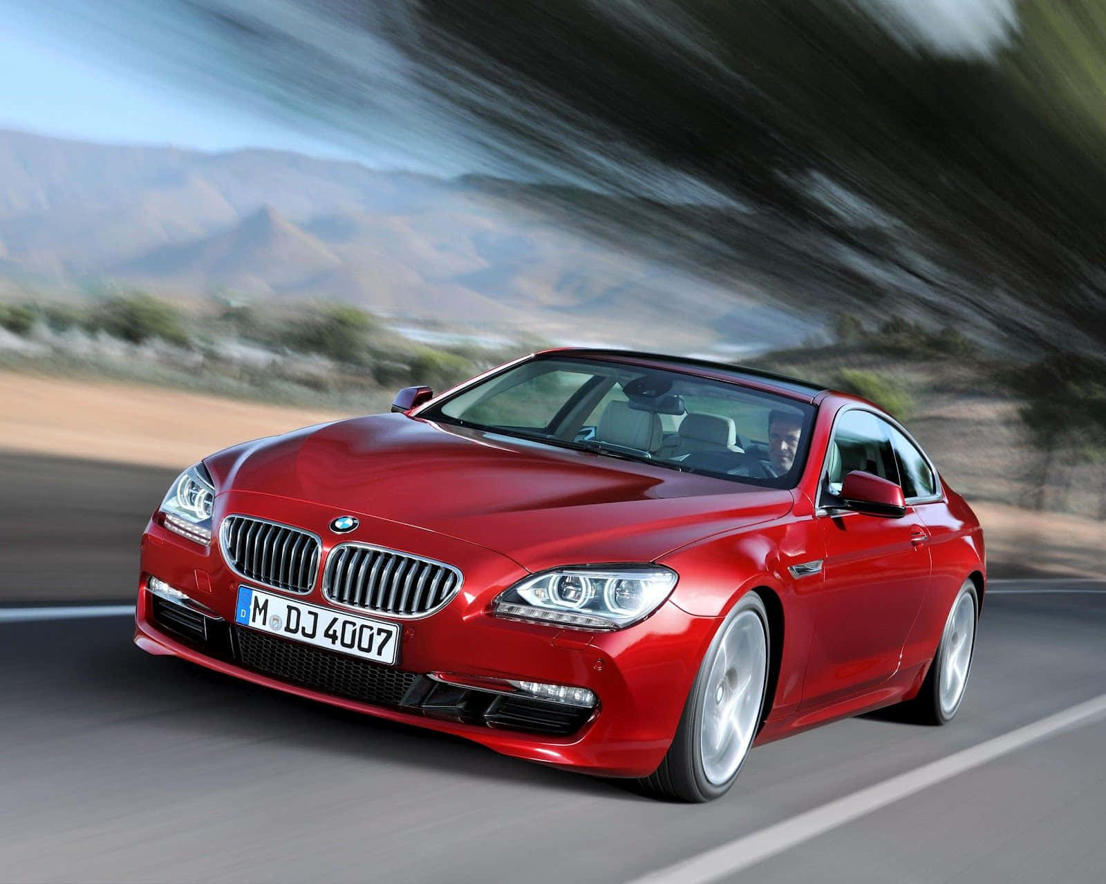 紅色BMW 6系雙門跑車在日落時分於山路上疾馳。