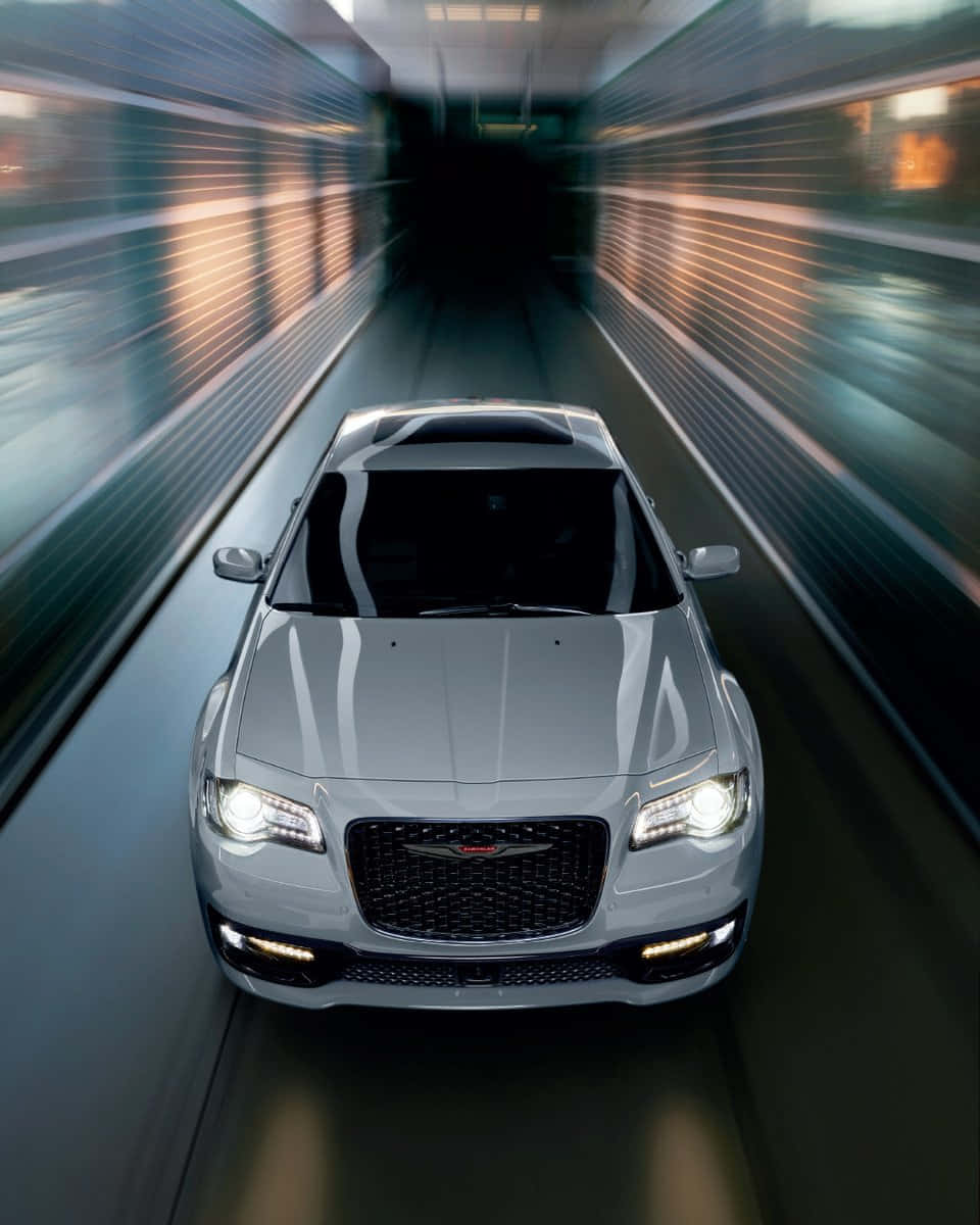 駕駛 Chrysler，暢遊城市奢華風景 壁紙 — 一輛銀色克萊斯勒轎車在隧道中飛馳，模糊的燈光掠過其發光的車頭燈。