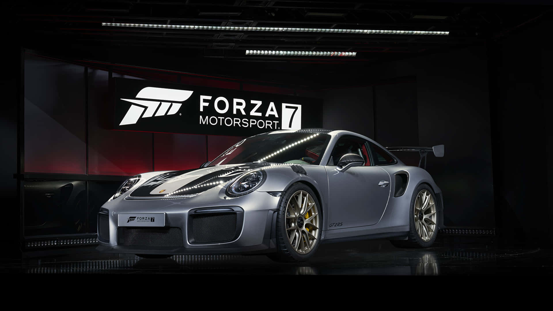 駕駛《Forza Motorsport 7》——最頂級賽車模擬器 壁紙 — 一輛時尚的銀色保時捷911 GT2 RS配金色輪圈，在工作室燈光下展示，背景為深色並帶有Forza Motorsport 7標誌。