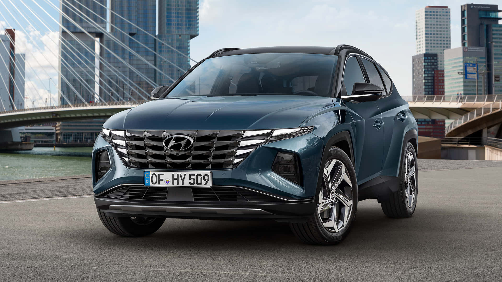 藍色現代 Tucson SUV 停泊在都市橋樑和高樓附近。