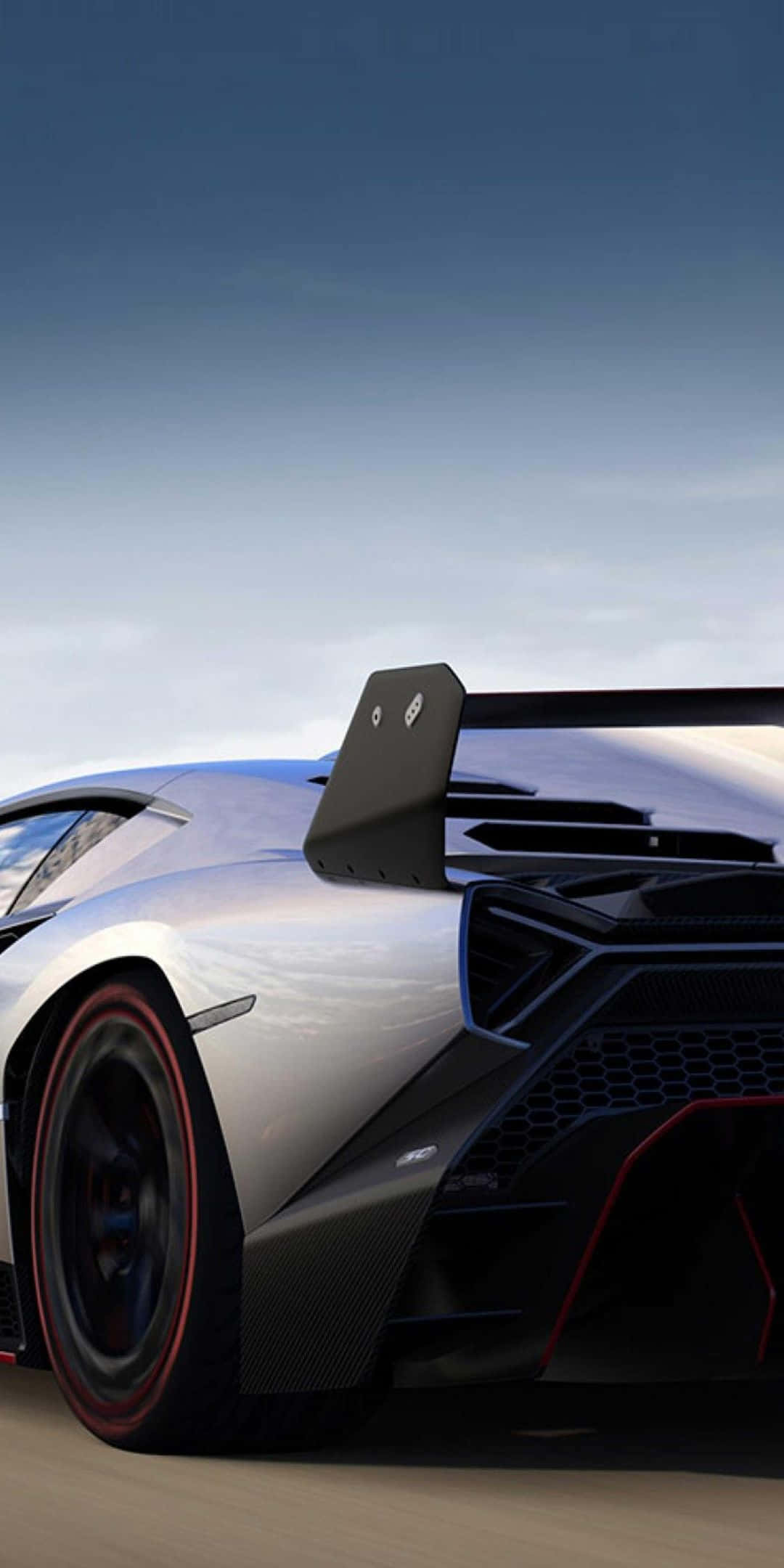 駕駛 Pixel 3 Lamborghini，享受開闊道路的自由 壁紙 — 一輛時尚的銀色林寶堅尼跑車，帶有黑色碳纖維飾邊和紅色點綴，在晴朗的藍天下沿著沙漠公路飛馳。