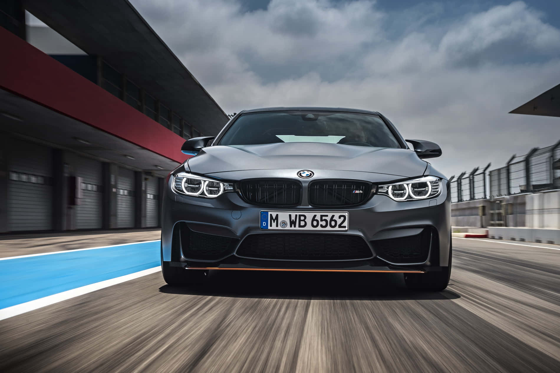 一輛灰色BMW M4在賽道上加速行駛，帶有動態模糊效果。