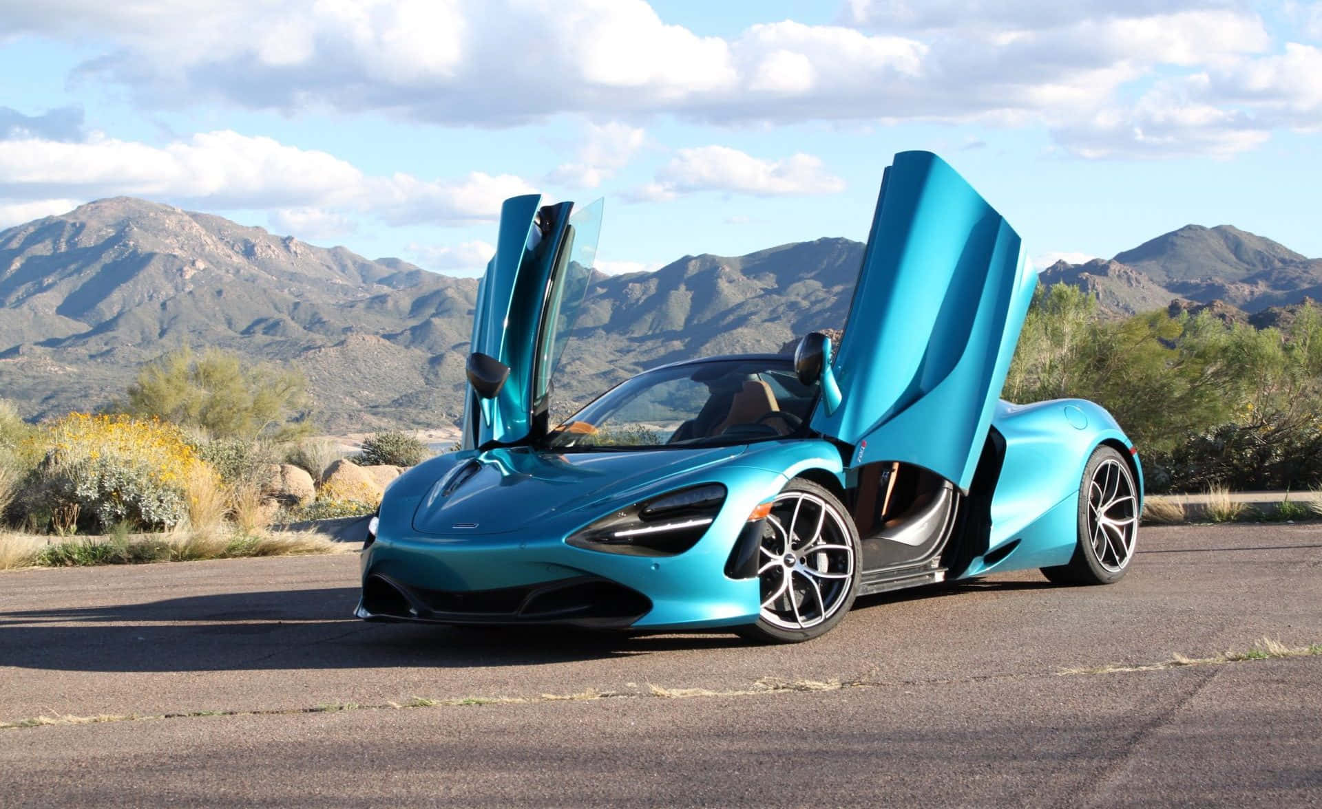 青綠色McLaren跑車在沙漠公路上打開鷗翼車門，靠近山脈。