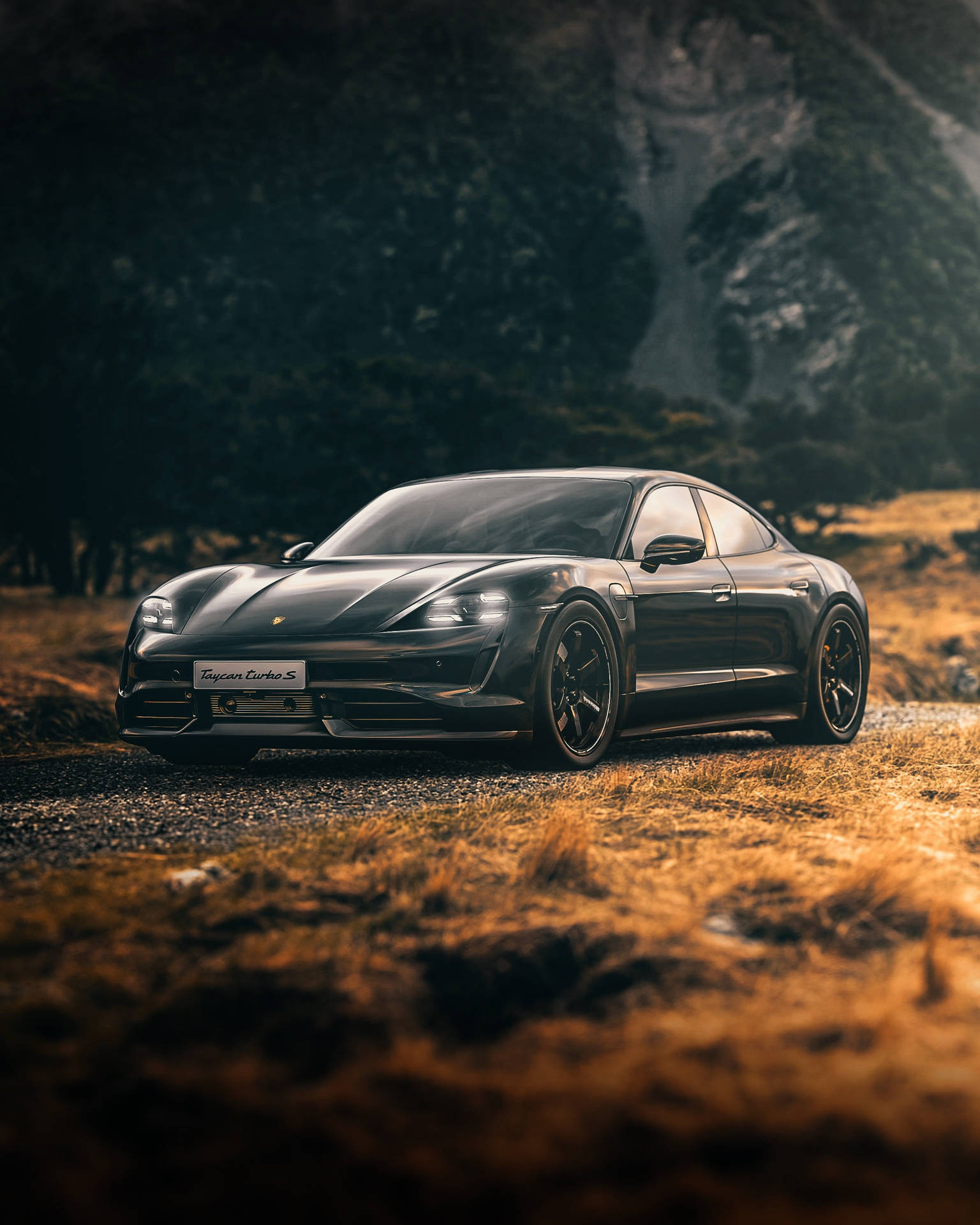 黑色保時捷 Taycan Turbo S 在黃金時刻停放在碎石路上，靠近森林覆蓋的山脈。