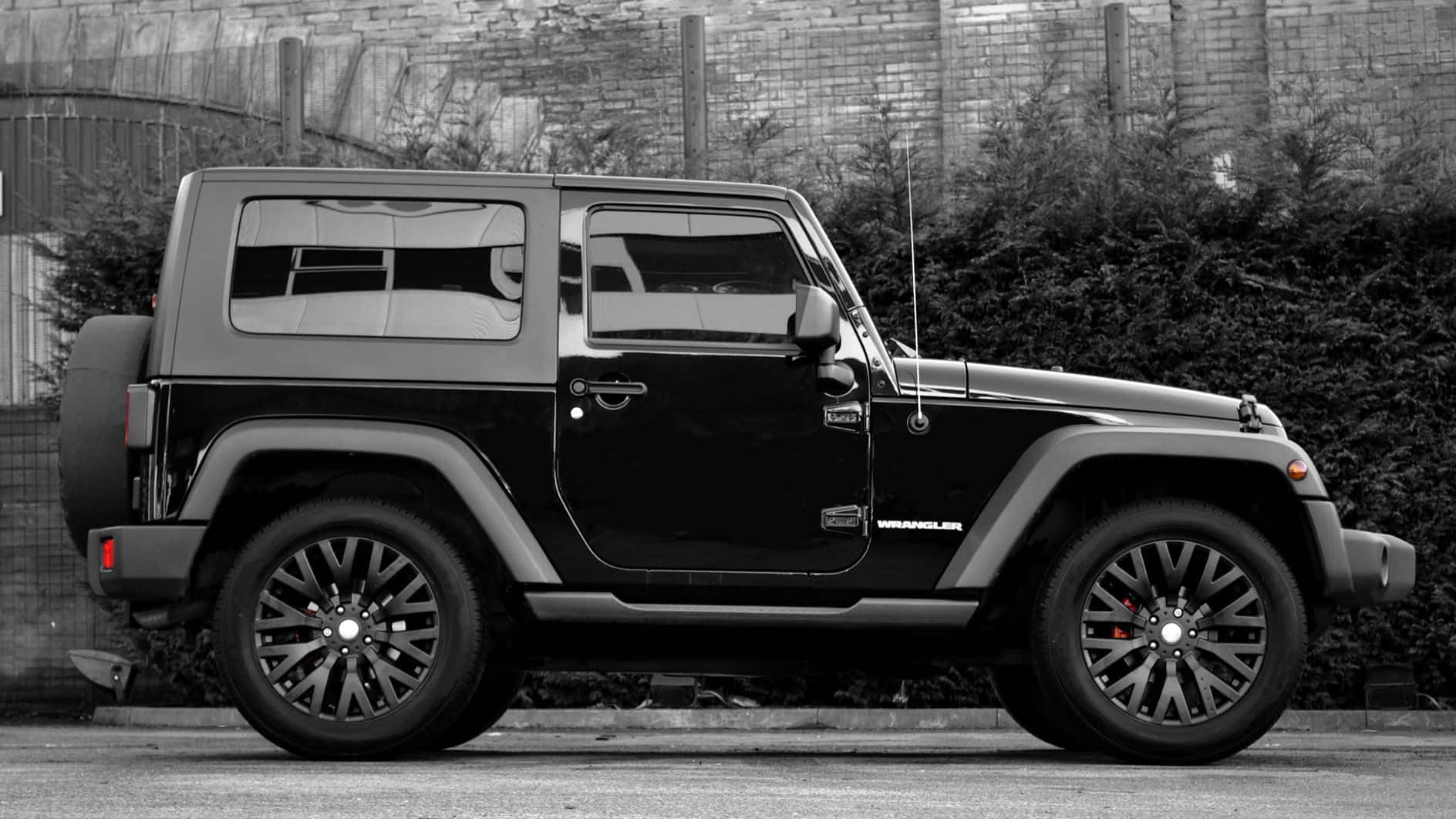 黑色Jeep Wrangler停在磚牆和灌木叢附近的街道上。