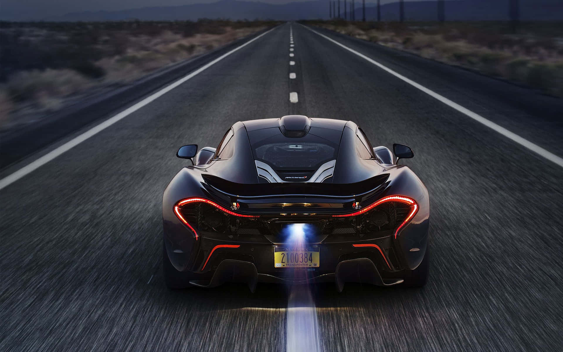 黑色McLaren P1在黃昏時分在沙漠高速公路上飛馳，帶有發光燈光。