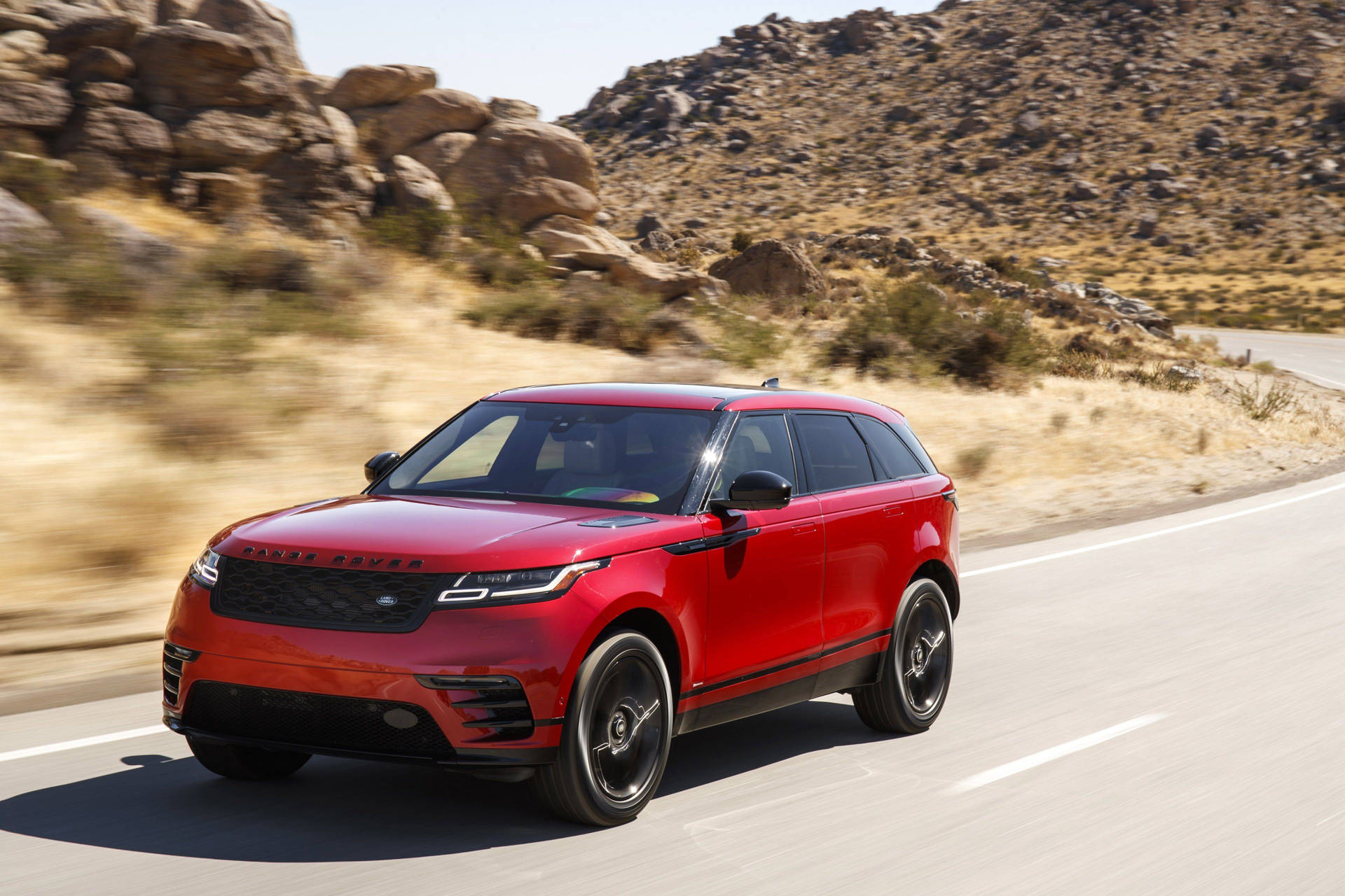 紅色Range Rover SUV在沙漠公路上行駛，地形多石。
