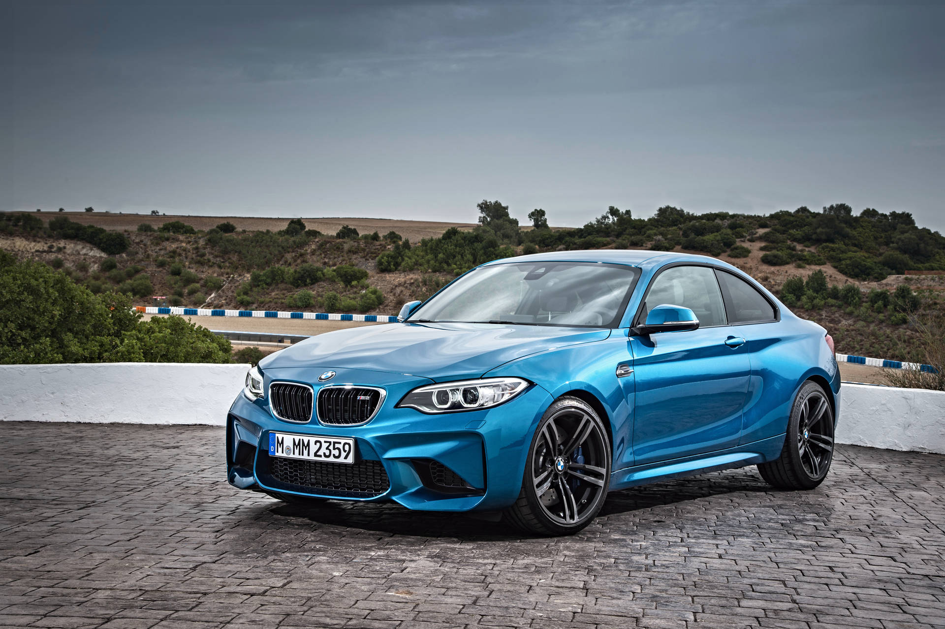 藍色BMW M2跑車停在石頭觀景點，後面有山丘。