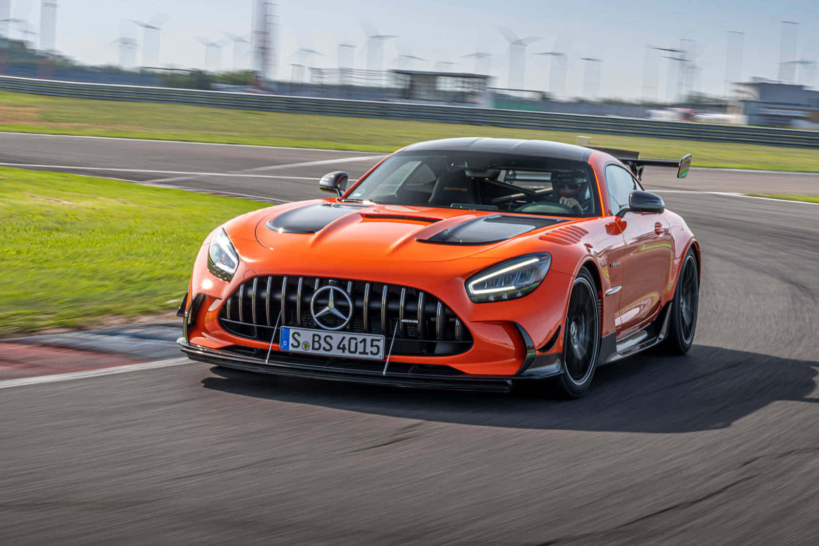 橙色 Mercedes-AMG GT R 在賽道上疾馳，背景有風力發電機。