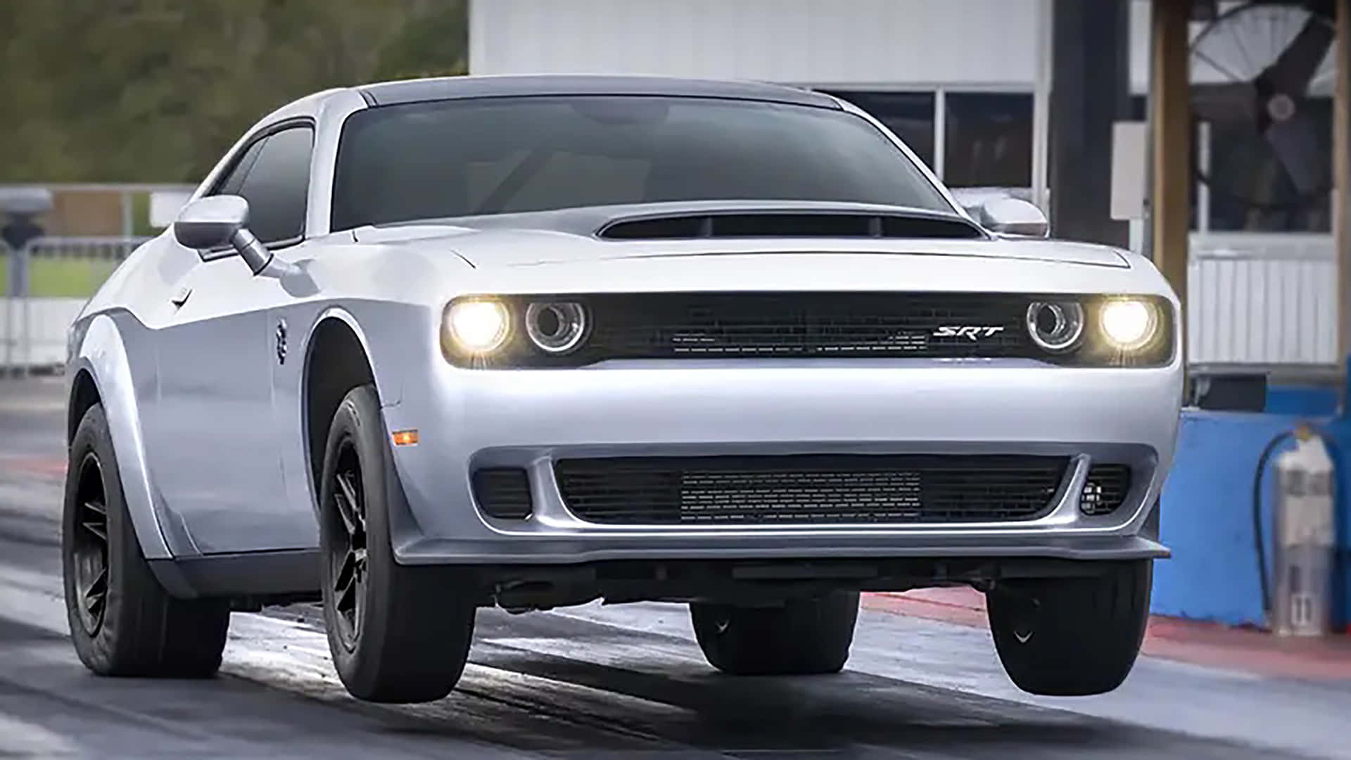 銀色Dodge Challenger SRT在潮濕的直線加速賽道上亮著車頭燈加速行駛。