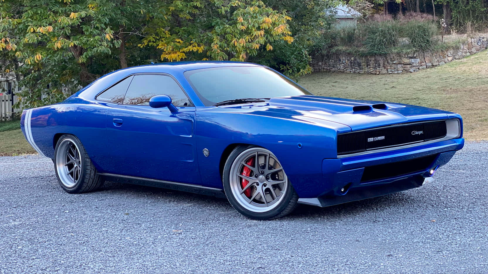 藍色Dodge Challenger停在碎石上，靠近秋樹和石牆。