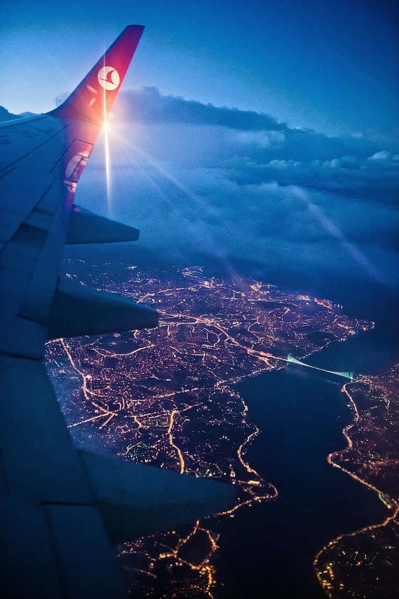 駕駛雄偉飛機翱翔天際 壁紙 — 飛機機翼在夕陽餘暉中閃耀，下方廣闊的城市景觀被金色燈光照亮。