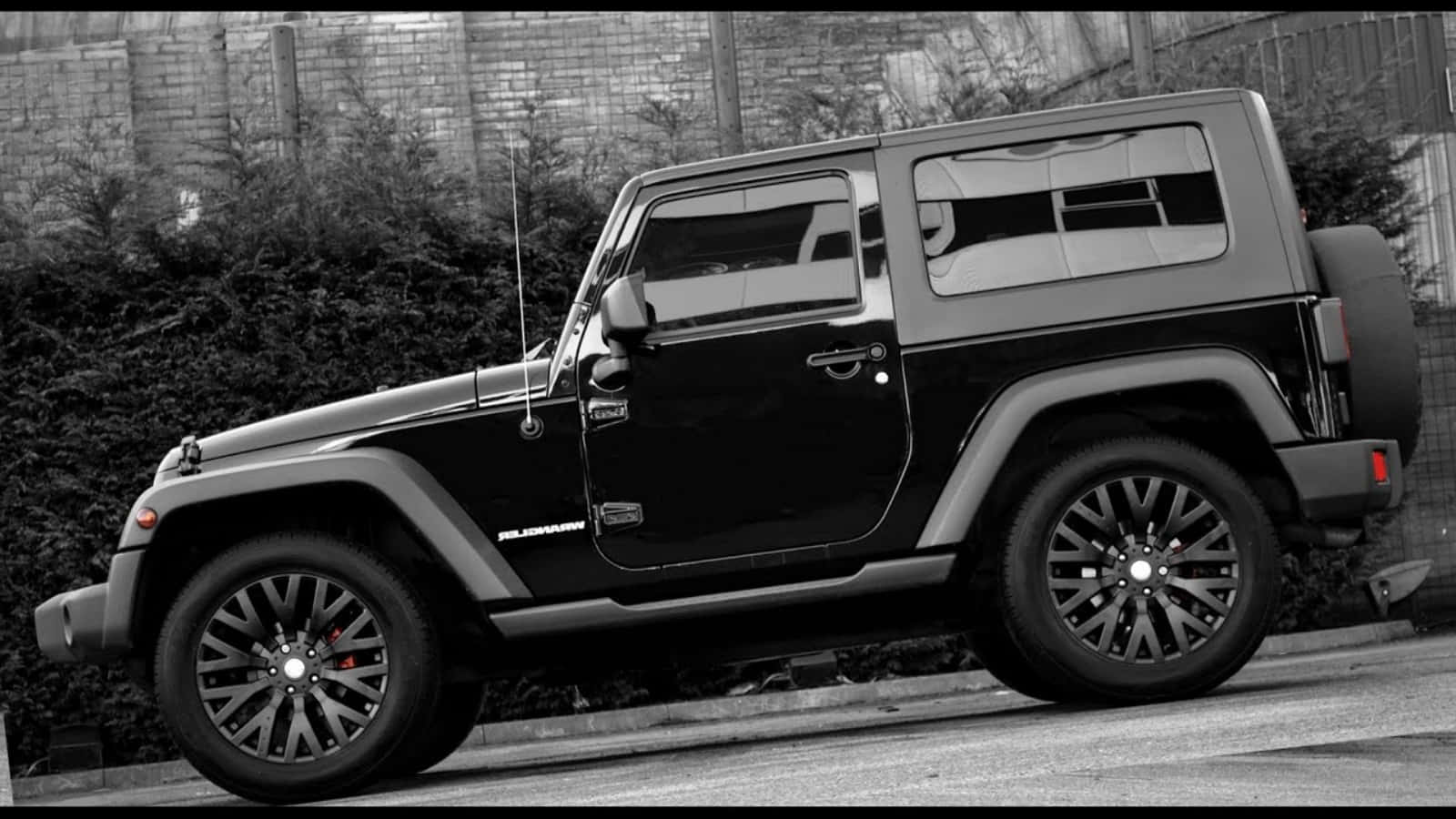 黑色Jeep Wrangler停泊在靠近磚牆和綠化的城市街道上。