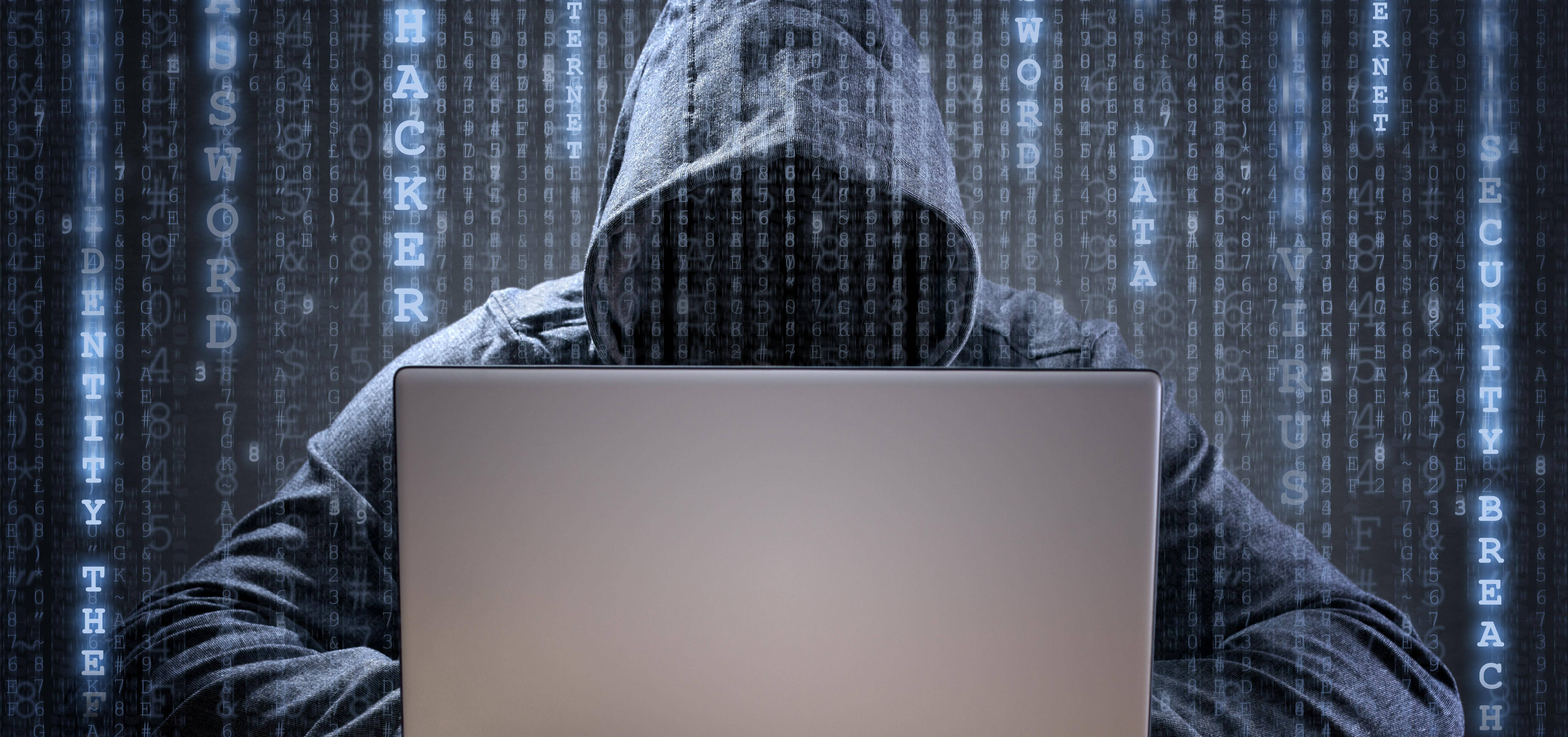 駭客穿越網路安全 壁紙 — 一名戴帽的黑客坐在筆記型電腦前，數位代碼在黑暗的賽博龐克環境中環繞著他們。