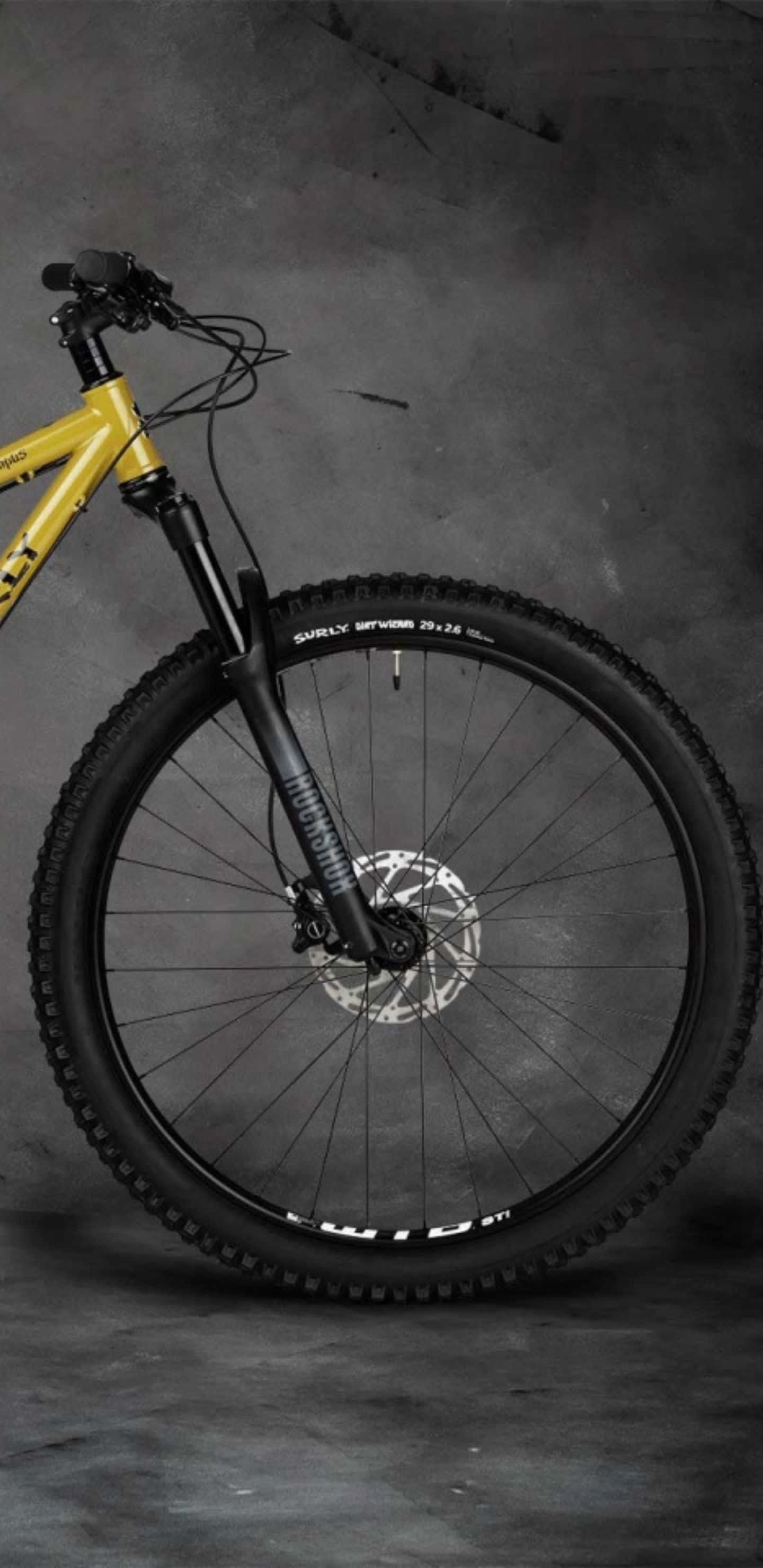 騎上 Pixel 3xl 自行車，感受風與速度 壁紙 — 一架搶眼的黃色爬山單車，配備黑色前叉和防滑輪胎，矗立在紋理灰色工作室背景前。