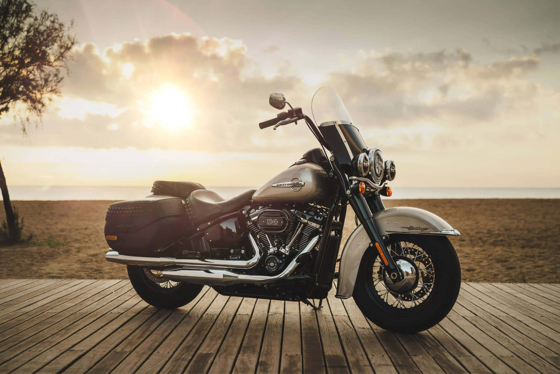 騎上HD機車，暢遊開闊道路 壁紙 — 一架時尚的黑色電單車停泊在木製碼頭上，夕陽的金色光芒在海面上投下長長的影子。