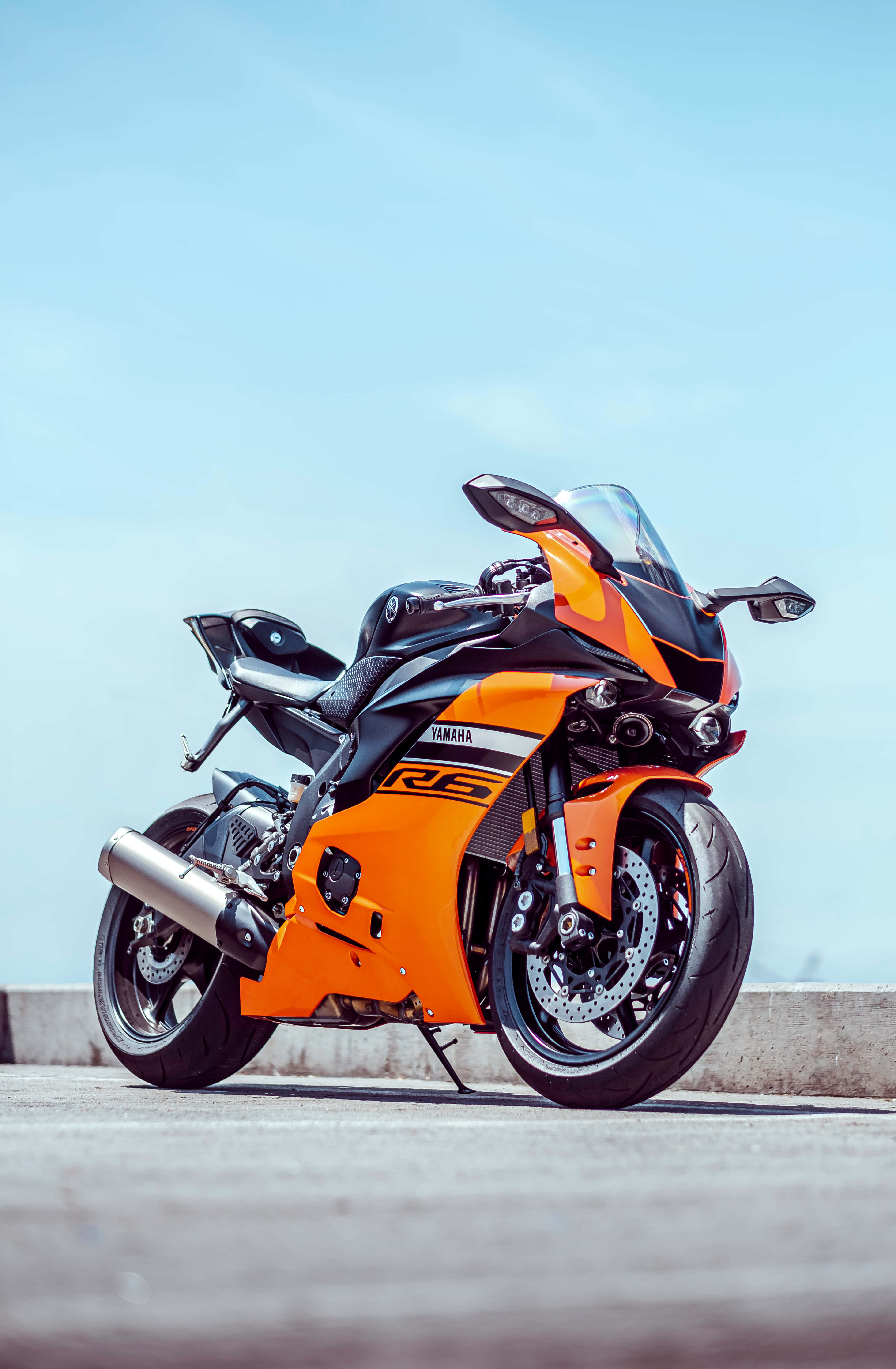騎上吧！ 壁紙 — 一輛鮮豔的橙色和黑色Yamaha R6運動摩托車停在混凝土表面上，天空湛藍清澈。