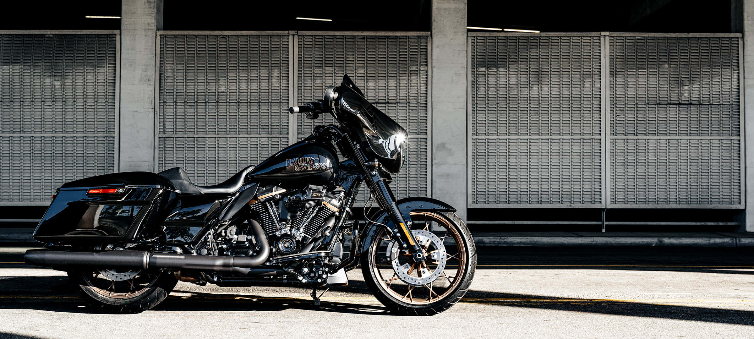 騎上哈雷戴維森，享受開闊道路 壁紙 — 一架時尚黑色Harley-Davidson電單車停泊在混凝土天橋下，背景有工業金屬圍欄。