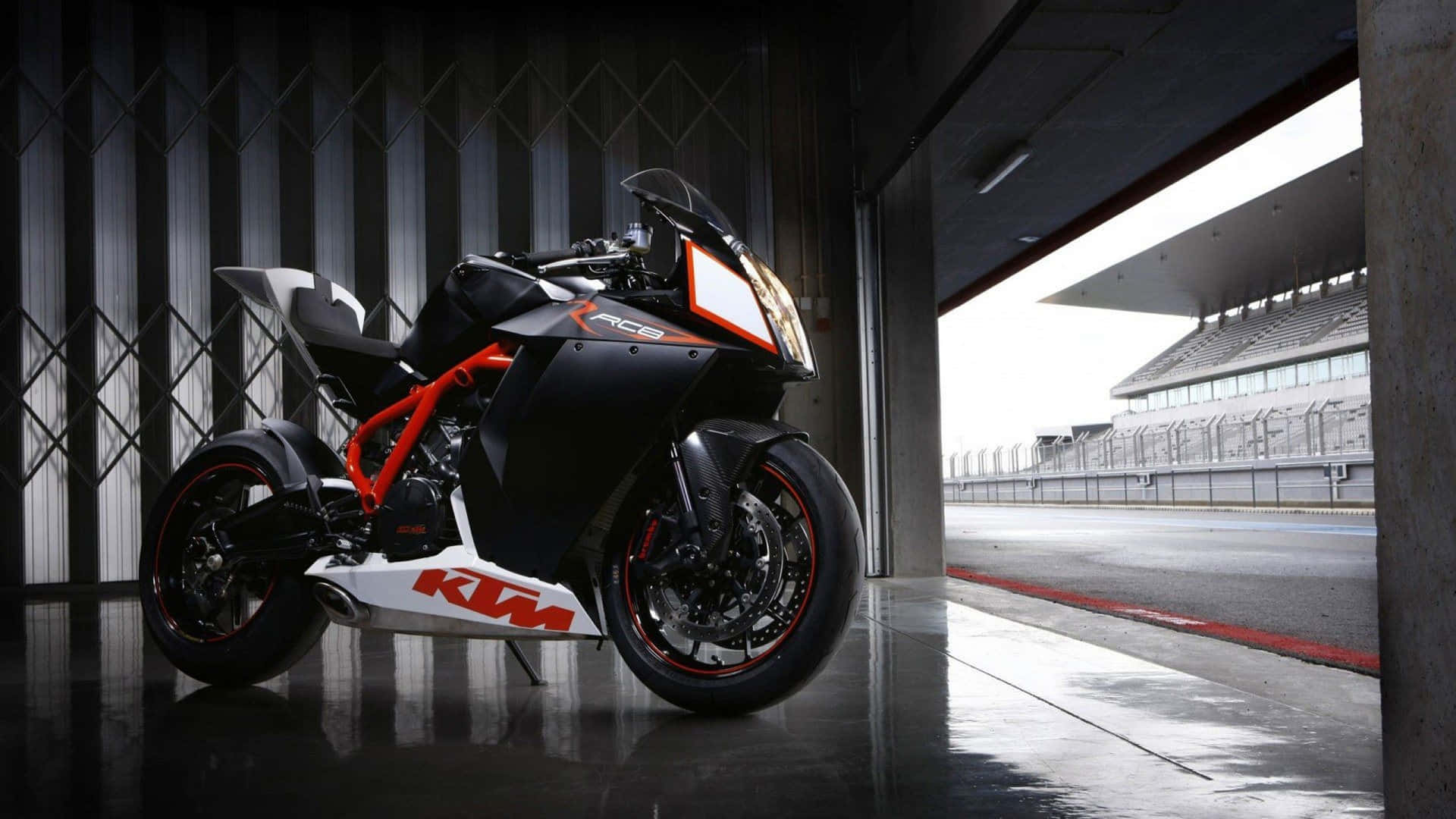 黑色和橙色KTM RC8R電單車停放在車庫，外面有賽道。