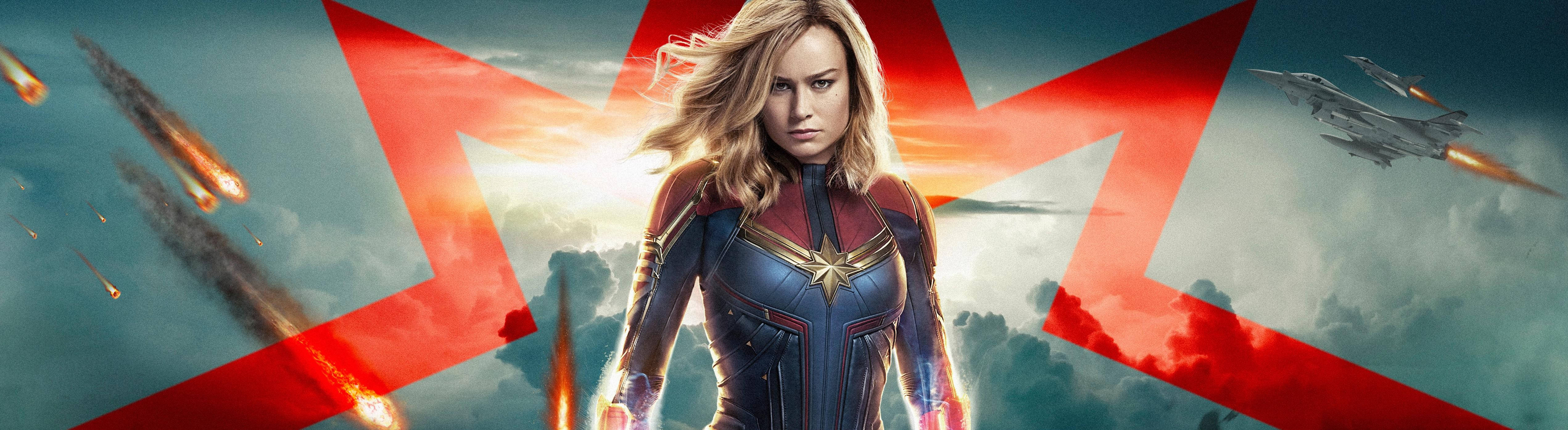Captain Marvel 5120 x 1440 壁紙 — 驚奇隊長在戲劇性的天空下，伴隨著紅色星爆、戰鬥機和墜落的流星，英勇地站立。