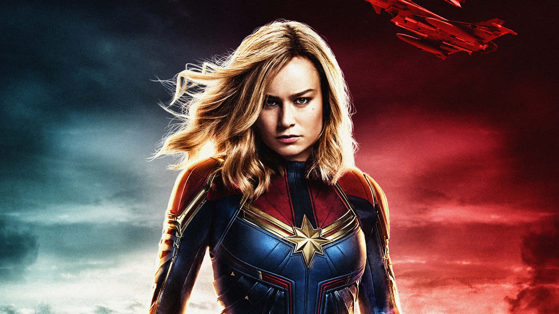 brie larson 桌布 壁紙 — 驚奇隊長身穿藍紅戰衣，在風暴雲和火紅能量劃破的戲劇性天空下堅定站立。